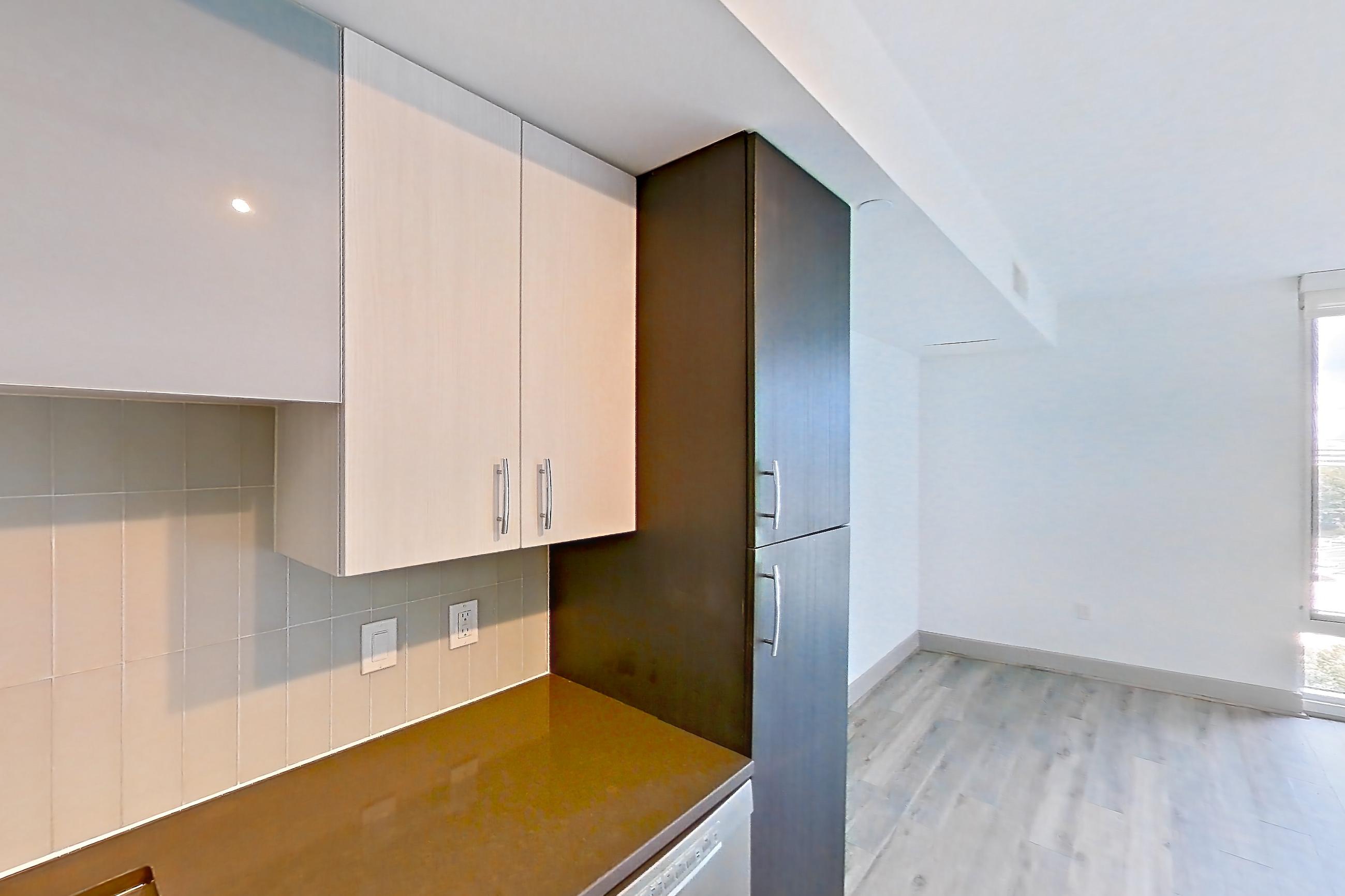 Kitchen with dark countertops, dark stone countertops, dishwasher, electric range, light countertops, light wood-finish flooring, microwave, oven/range, refrigerator, stainless steel appliances, and white appliances, Apartment 906 at Adaire