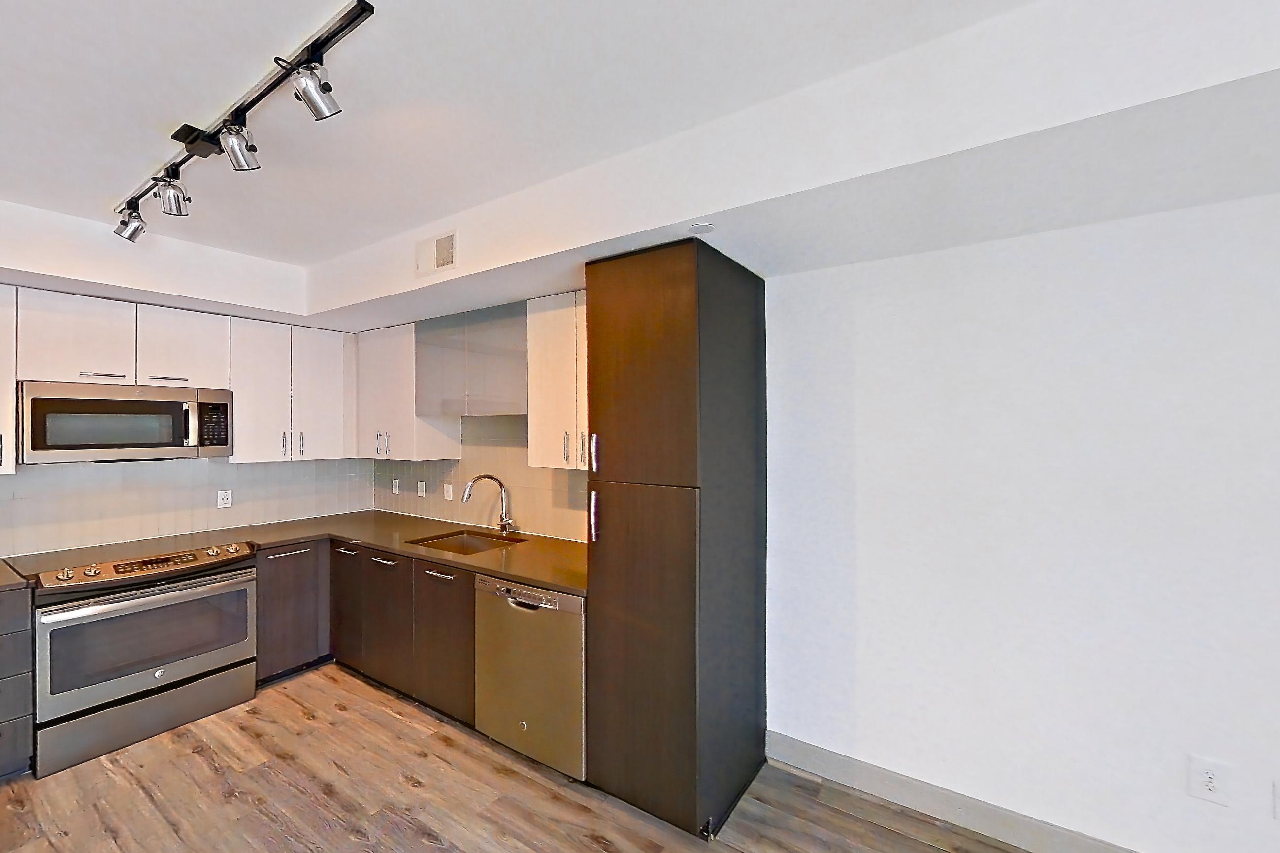 Living room with dark countertops, dishwasher, light wood-finish flooring, and stainless steel appliances, Apartment 906 at Adaire