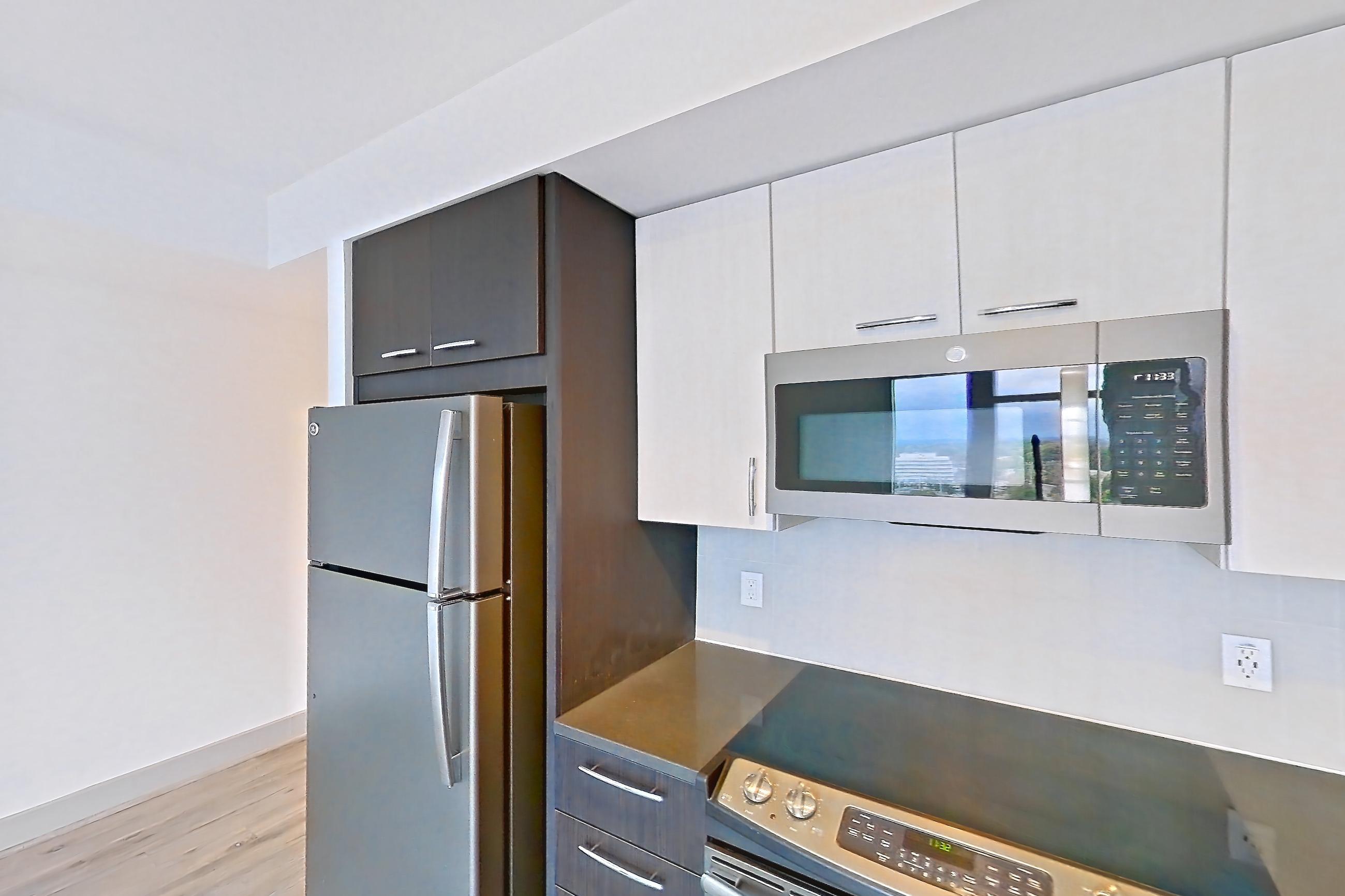 Kitchen with dark countertops, dark stone countertops, dishwasher, electric range, light wood-finish flooring, microwave, oven/range, refrigerator, stainless steel appliances, and white appliances, Apartment 1606 at Adaire