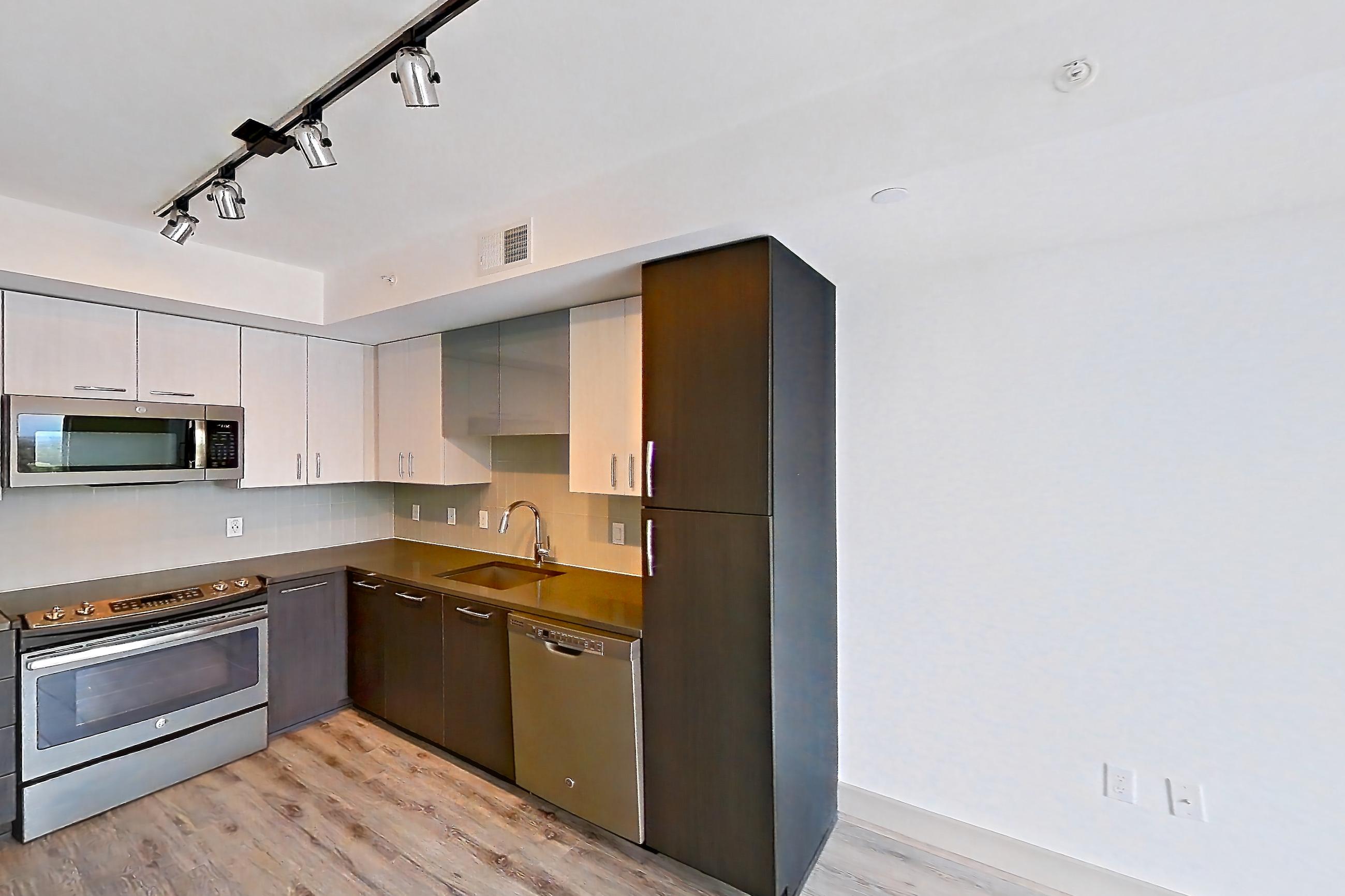 Living room with dark countertops, dishwasher, light wood-finish flooring, and stainless steel appliances, Apartment 1606 at Adaire