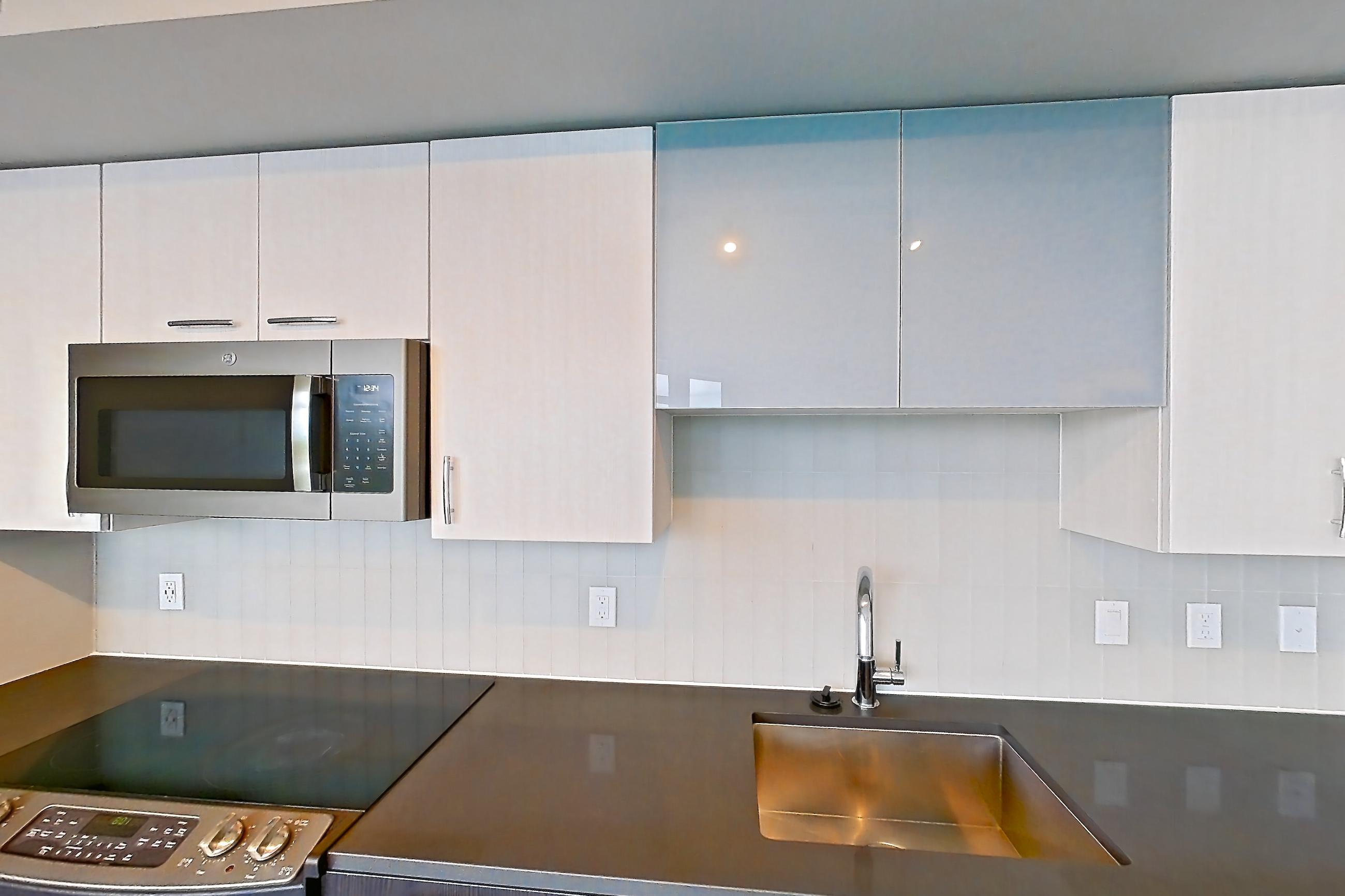 Kitchen with dark countertops, dishwasher, electric range, light countertops, light wood-finish flooring, microwave, oven/range, refrigerator, and stainless steel appliances, Apartment 902 at Adaire