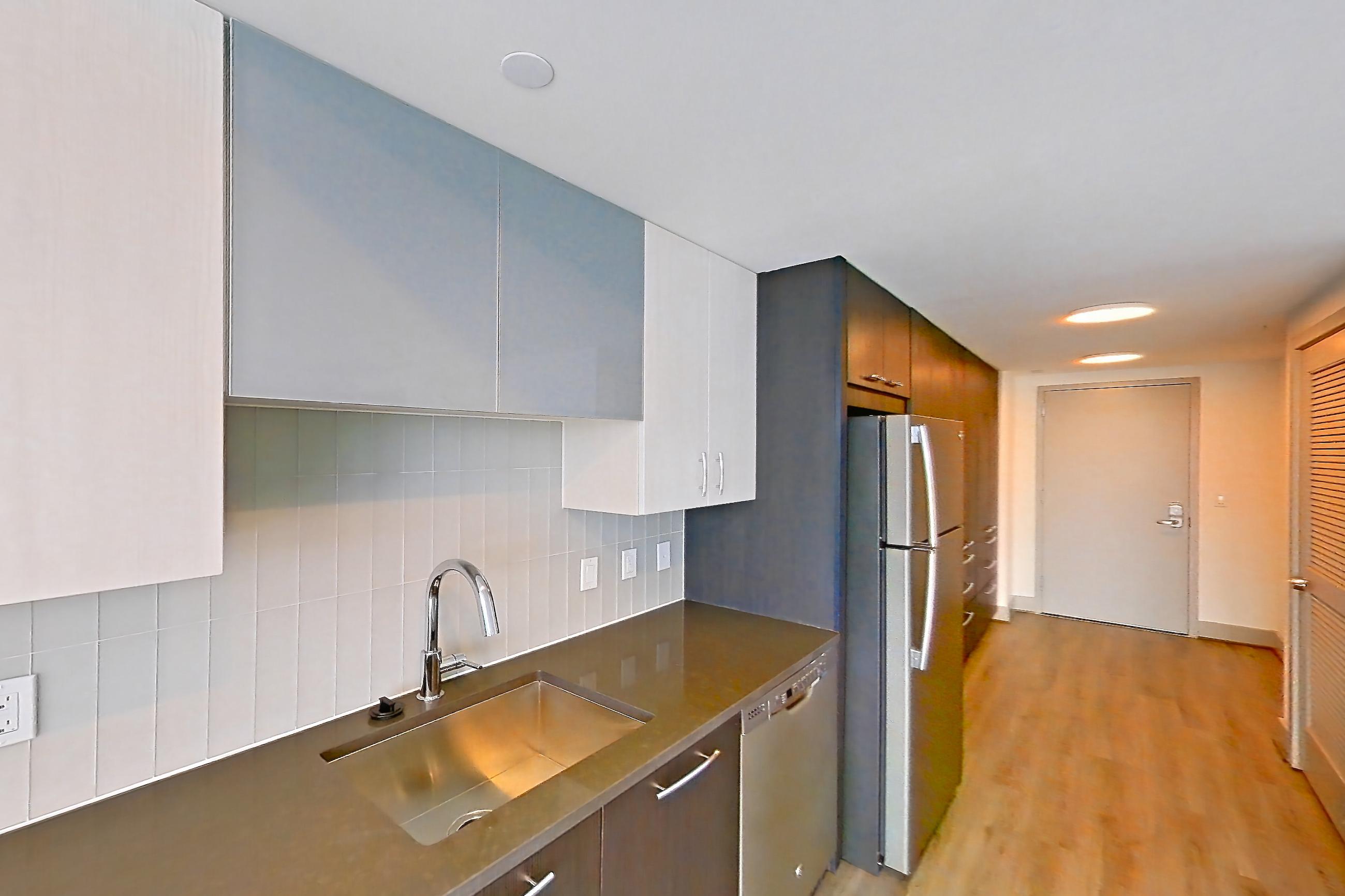 Kitchen with cooktop, dark countertops, dishwasher, electric cooktop, electric range, light countertops, light wood-finish flooring, microwave, oven/range, refrigerator, stainless steel appliances, and white appliances, Apartment 1303 at Adaire