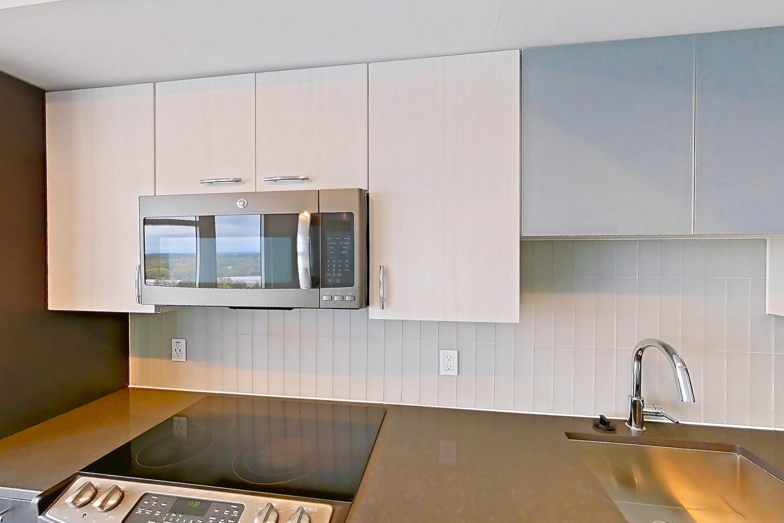 Kitchen with cooktop, dark countertops, dishwasher, electric cooktop, electric range, light countertops, light wood-finish flooring, microwave, oven/range, refrigerator, stainless steel appliances, and white appliances, Apartment 1303 at Adaire