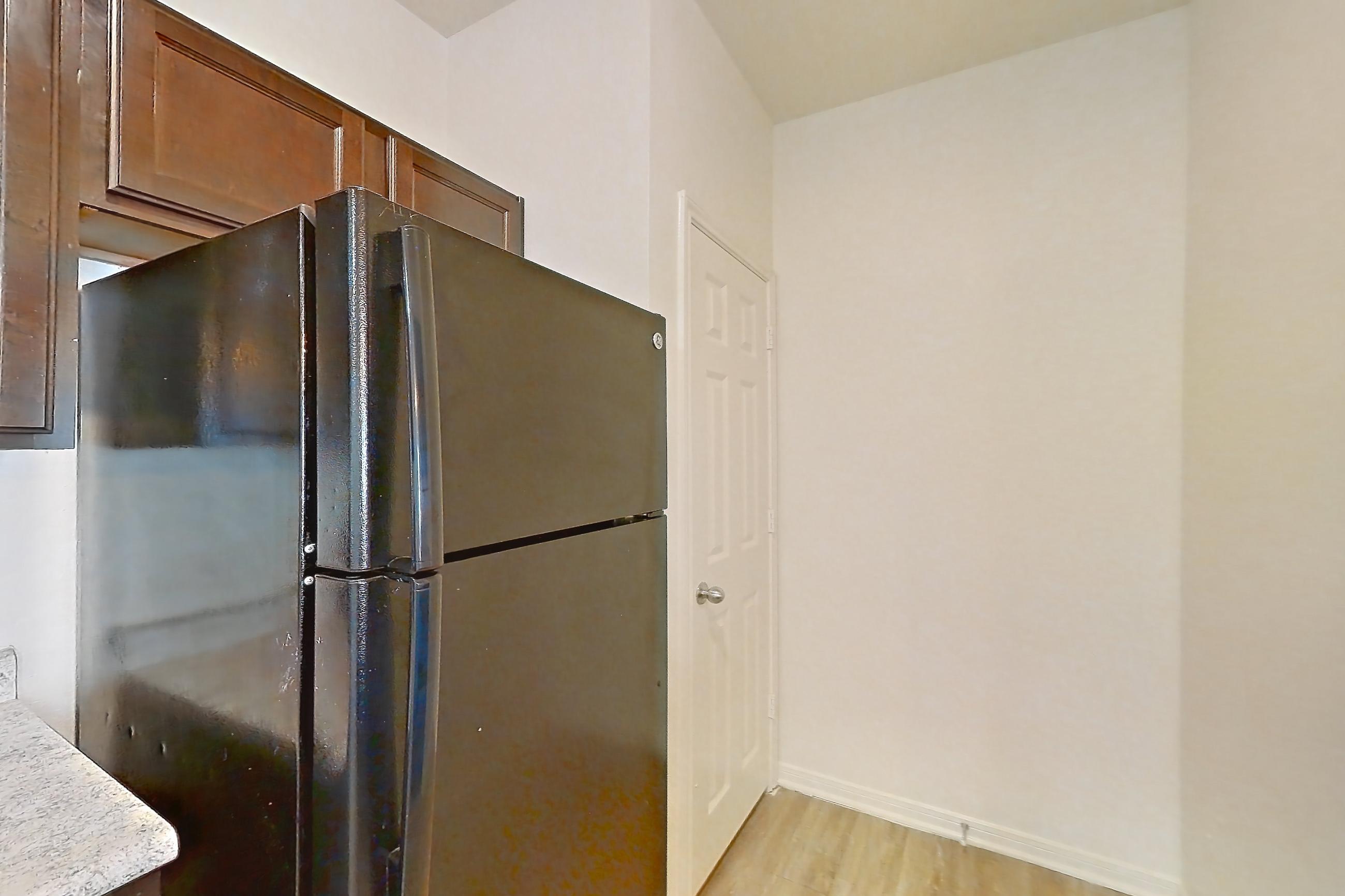 Kitchen with black appliances, electric range, light countertops, light stone countertops, light wood-finish flooring, oven/range, refrigerator, and stainless steel appliances, Apartment 913 at Tuckaway