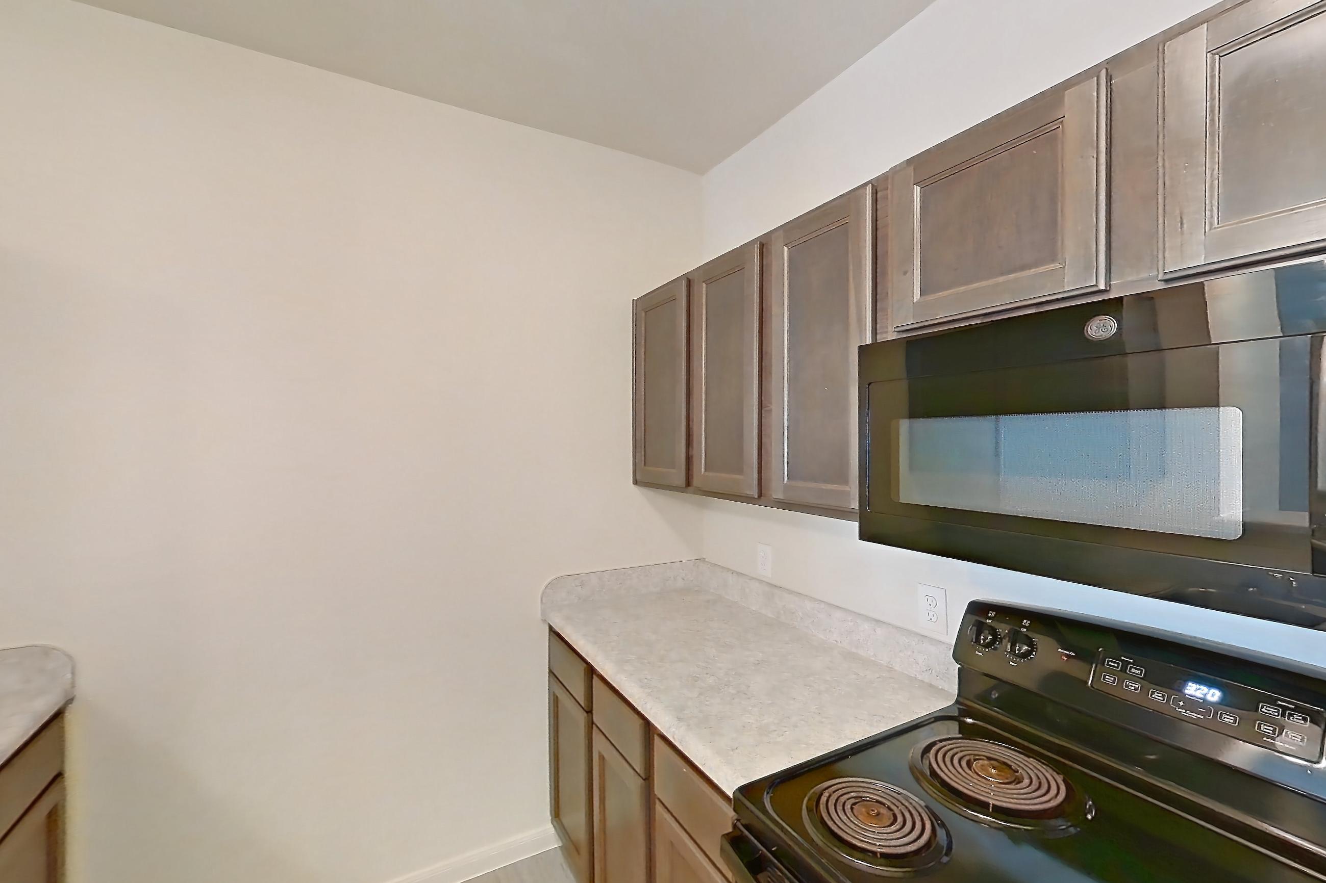 Kitchen with black appliances, dishwasher, electric range, light countertops, light wood-finish flooring, oven/range, refrigerator, and stainless steel appliances, Apartment 10208 at Denton Grove