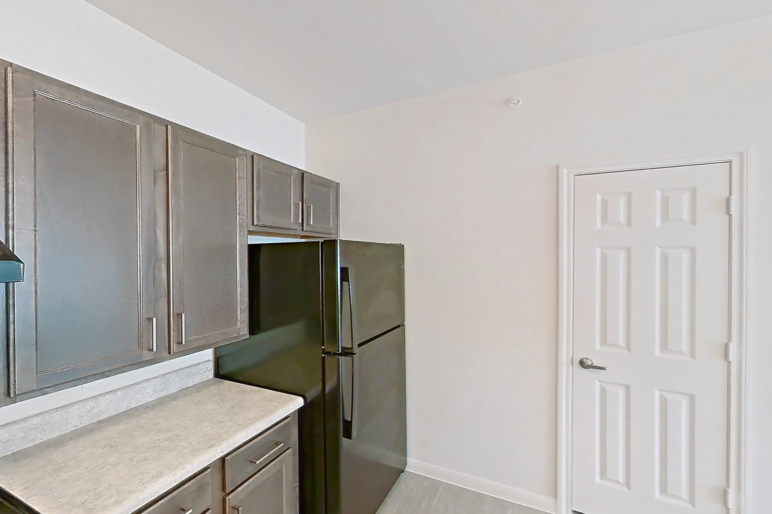 Kitchen with black appliances, electric range, light countertops, light wood-finish flooring, microwave, oven/range, and refrigerator, Apartment 8104 at Denton Grove