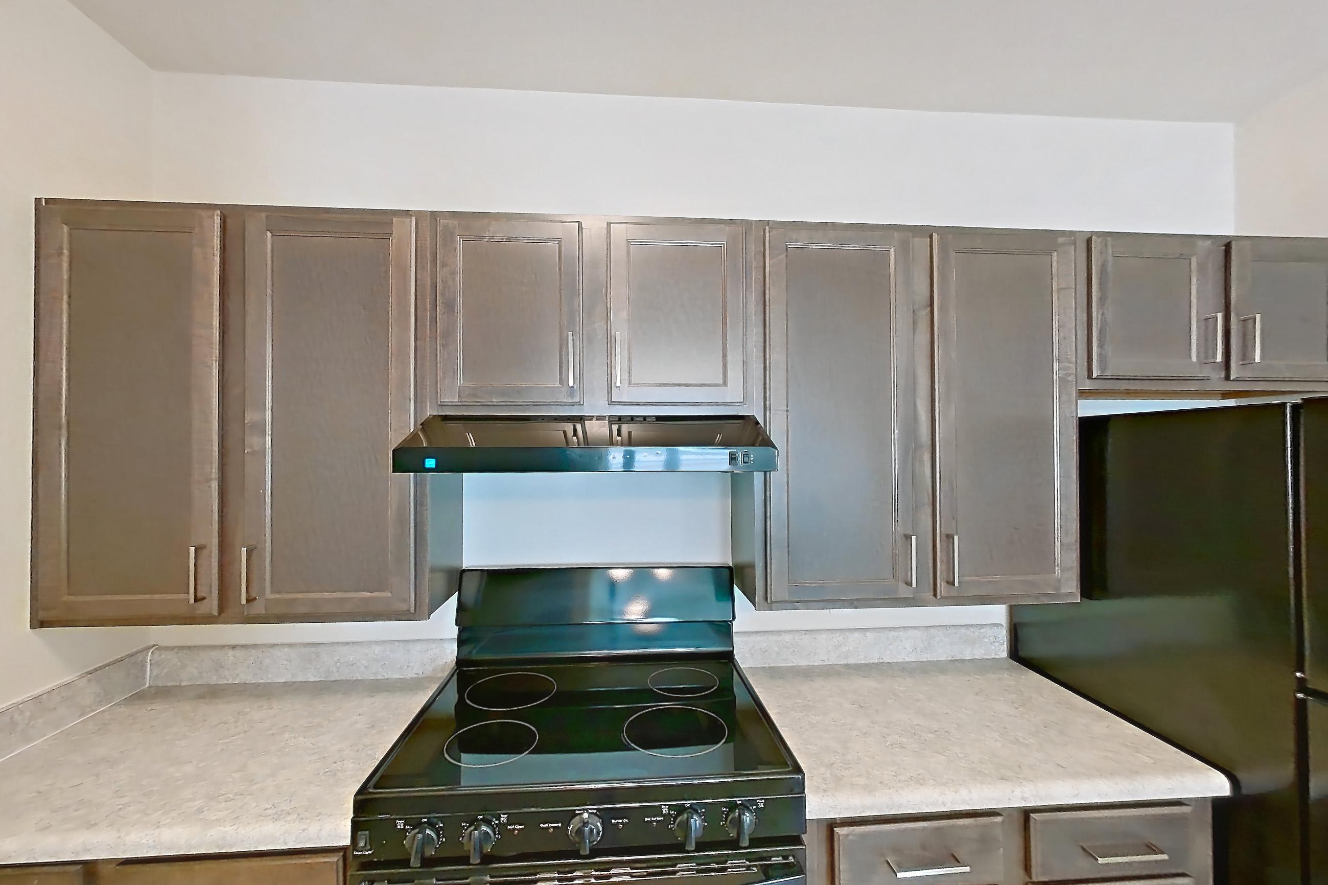 Kitchen with black appliances, electric range, light countertops, light wood-finish flooring, microwave, oven/range, and refrigerator, Apartment 8104 at Denton Grove