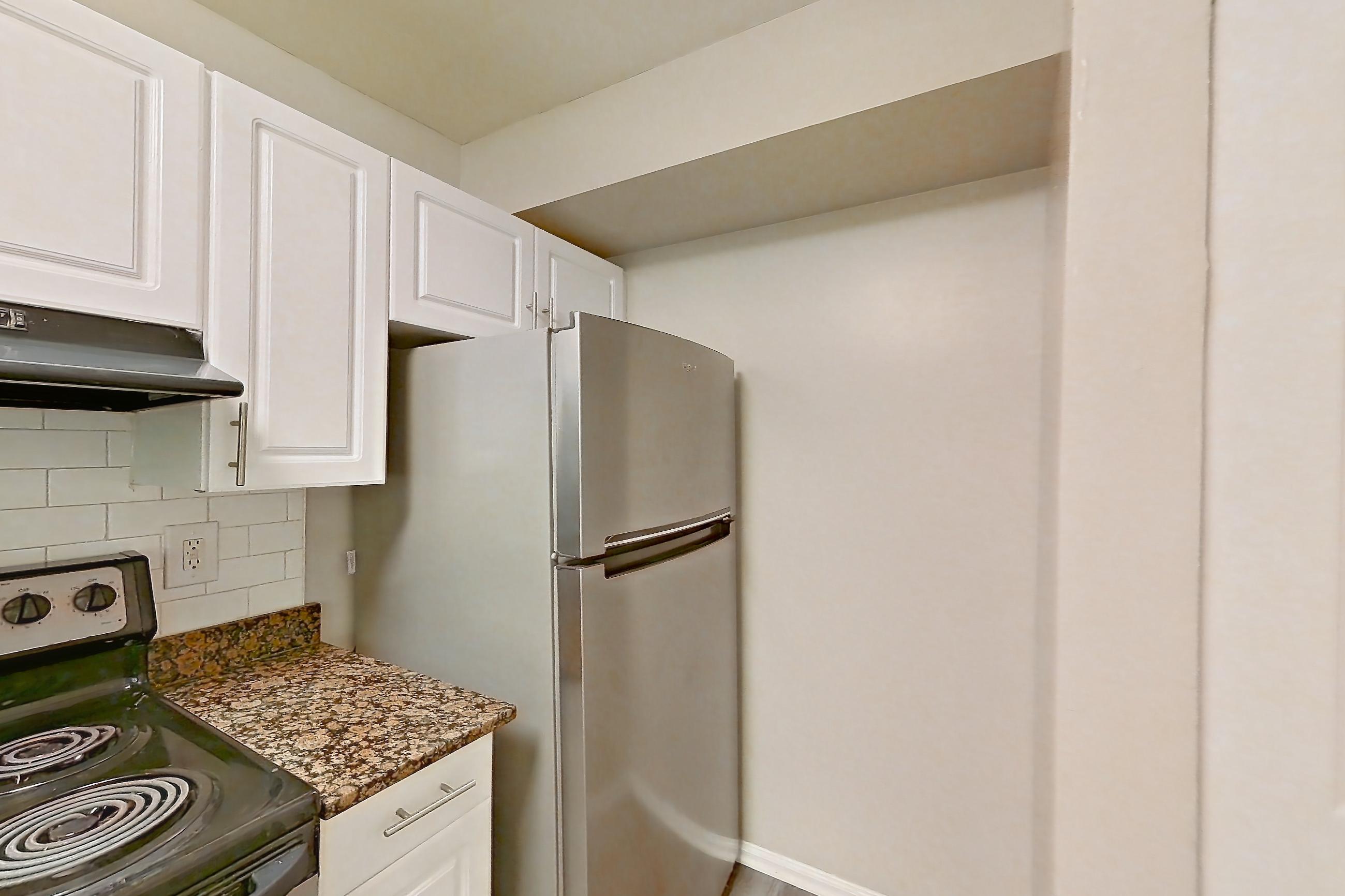 Kitchen with dark stone countertops, dishwasher, electric range, light countertops, light stone countertops, light wood-finish flooring, oven/range, range hood, refrigerator, stainless steel appliances, and white appliances, Apartment 3558W at The Ashford