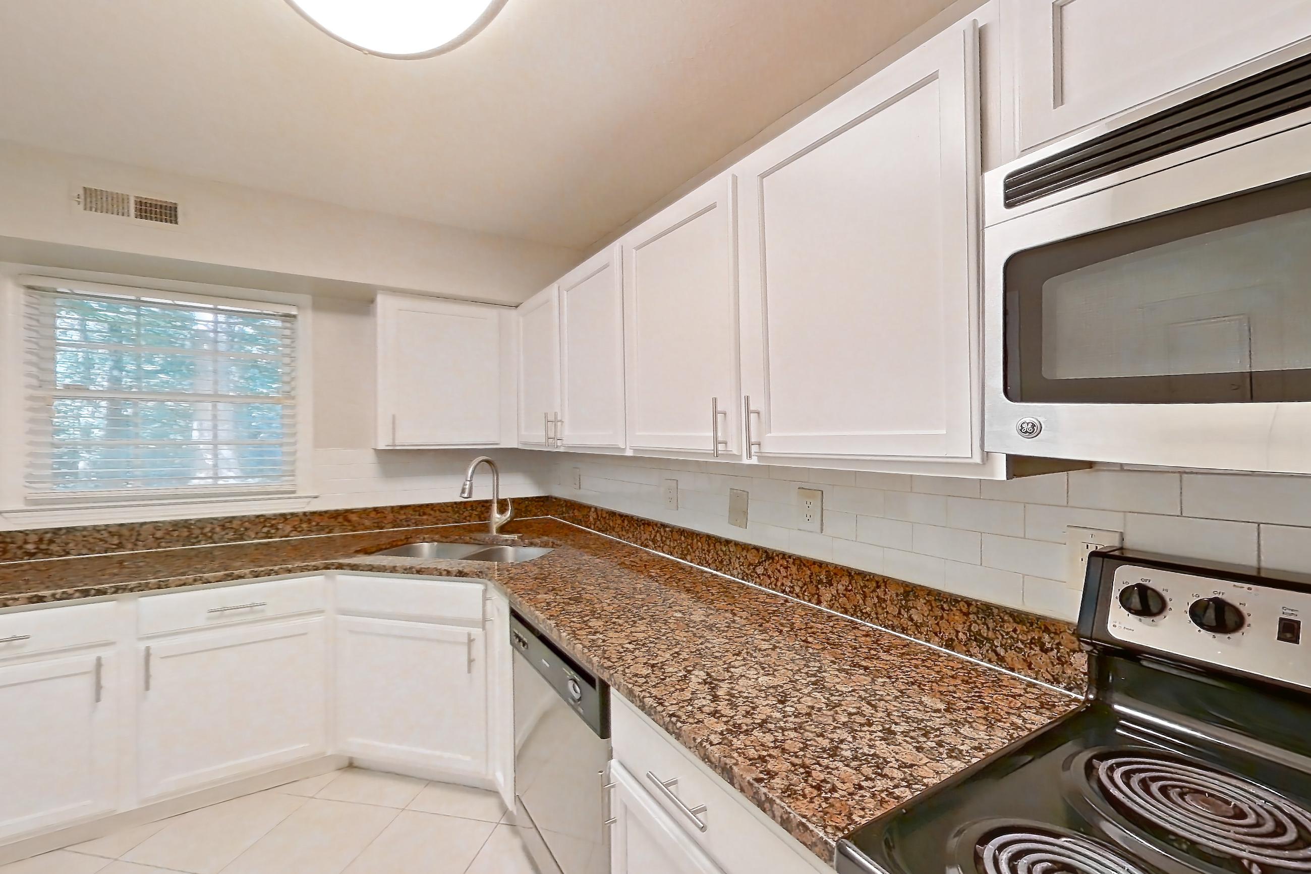 Kitchen with black appliances, dark stone countertops, dishwasher, electric range, light countertops, light tile flooring, microwave, oven/range, refrigerator, and stainless steel appliances, Apartment 1930A at The Ashford