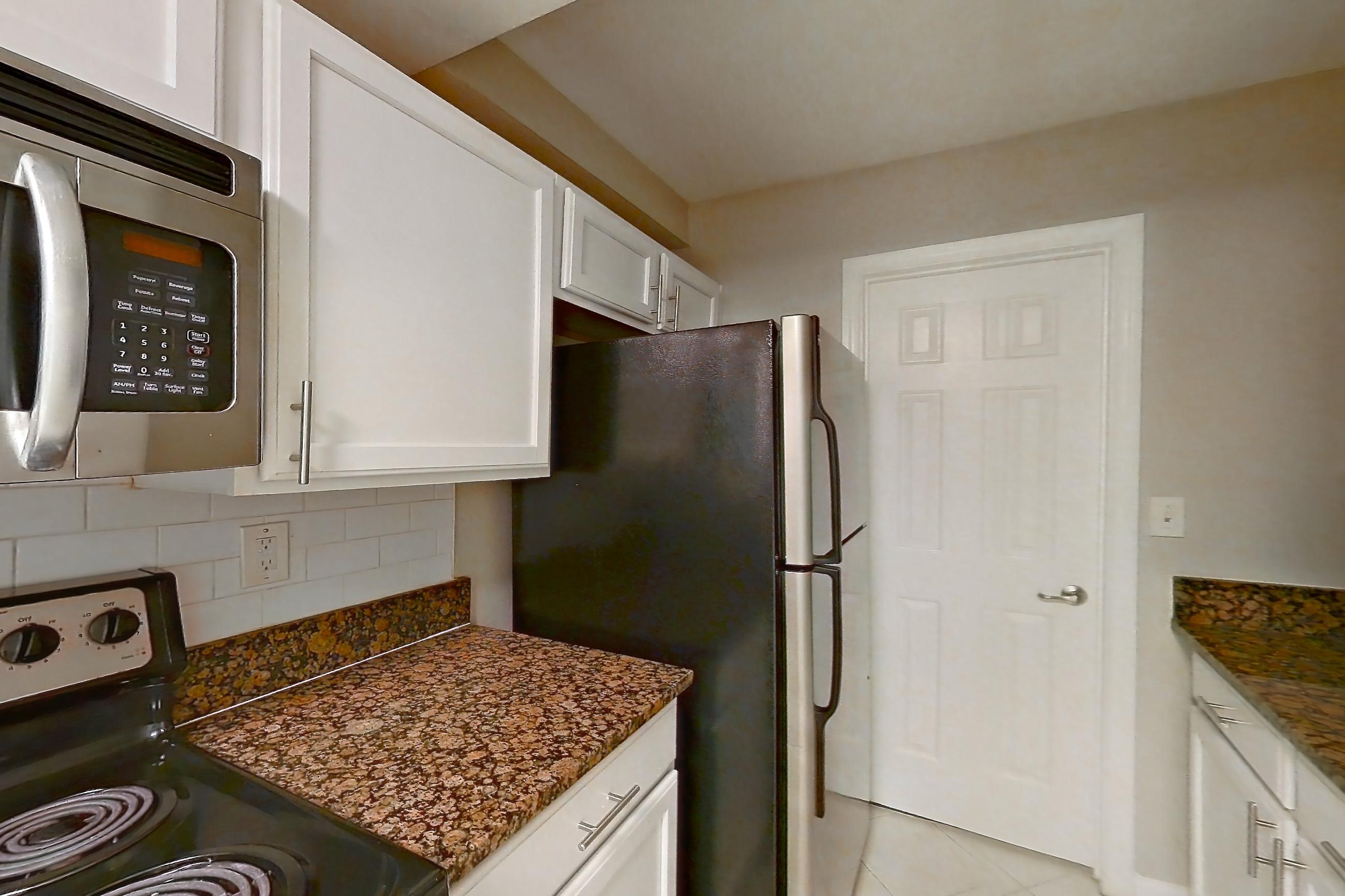 Kitchen with black appliances, dark stone countertops, dishwasher, electric range, light countertops, light tile flooring, microwave, oven/range, refrigerator, and stainless steel appliances, Apartment 1930A at The Ashford