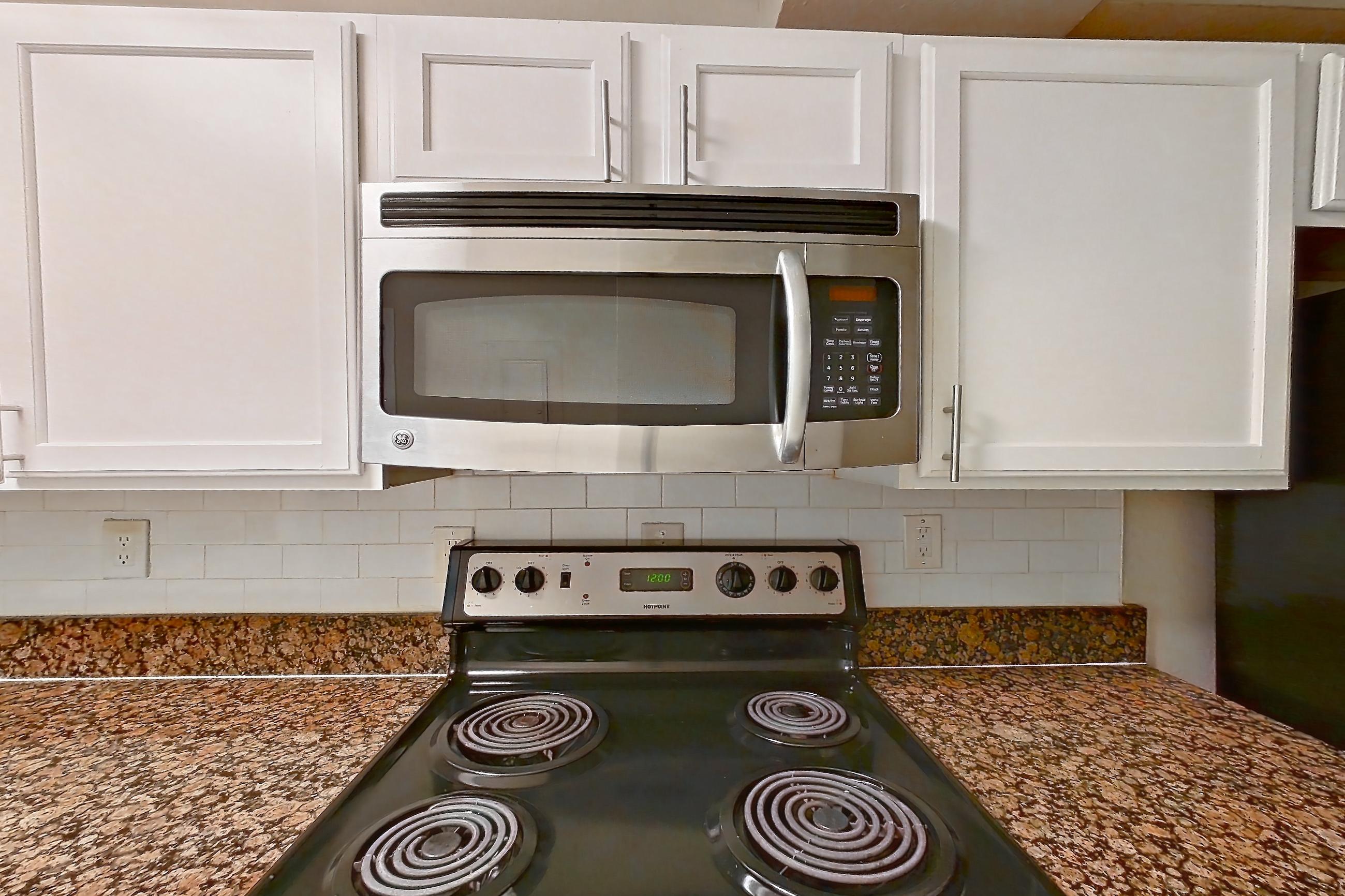Kitchen with black appliances, dark stone countertops, dishwasher, electric range, light countertops, light tile flooring, microwave, oven/range, refrigerator, and stainless steel appliances, Apartment 1930A at The Ashford