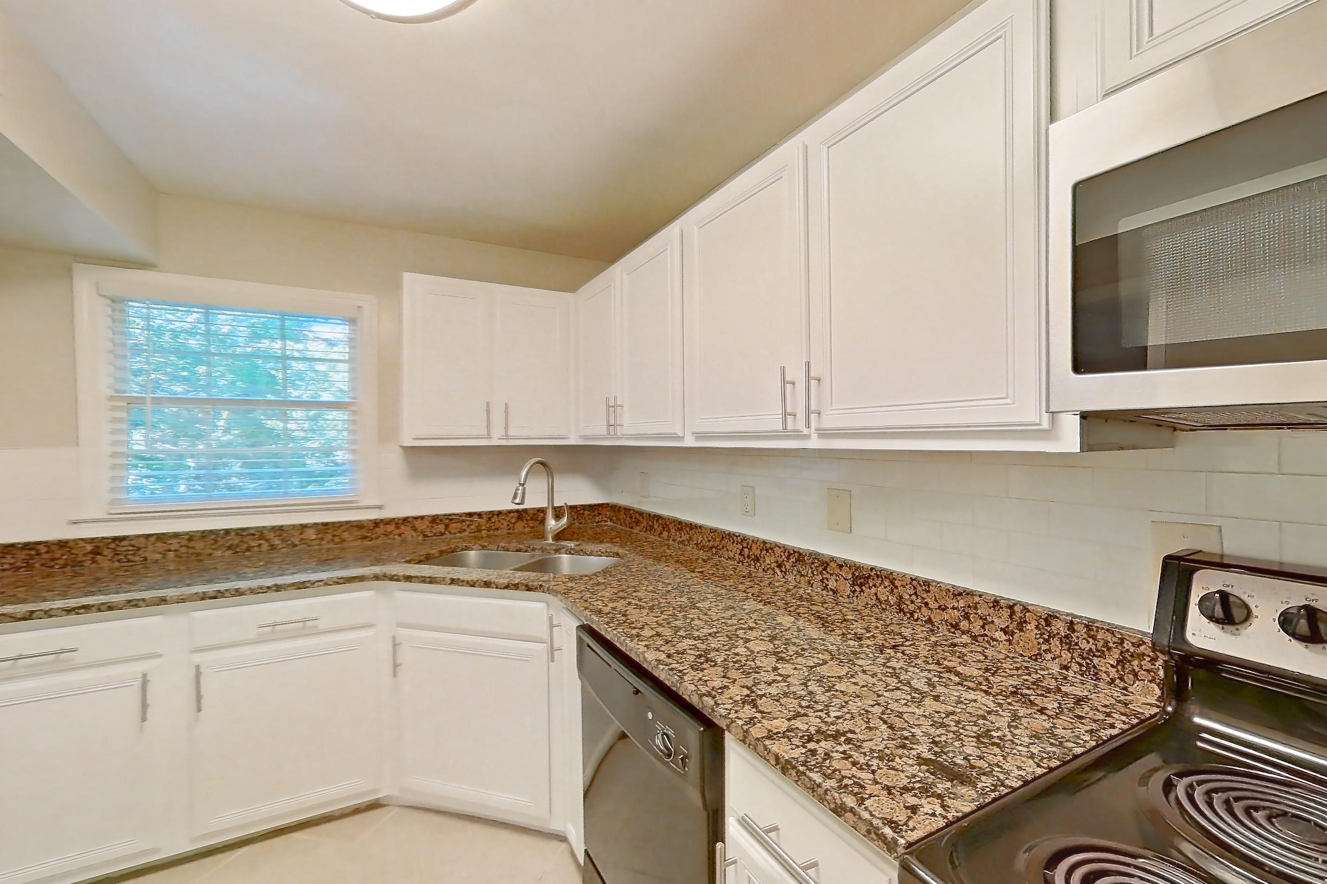 Kitchen with black appliances, dark stone countertops, dishwasher, electric range, light countertops, light tile flooring, microwave, oven/range, refrigerator, and stainless steel appliances, Apartment 3558Q at The Ashford