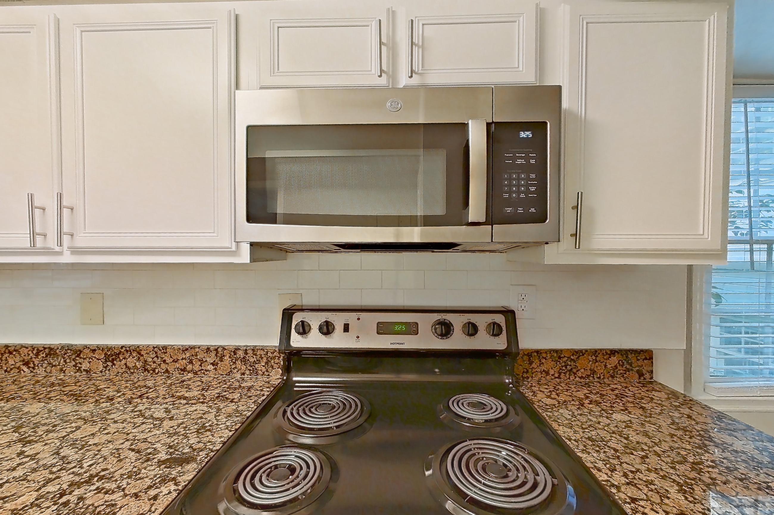 Kitchen with black appliances, dark stone countertops, dishwasher, electric range, light countertops, light tile flooring, microwave, oven/range, refrigerator, and stainless steel appliances, Apartment 3558Q at The Ashford