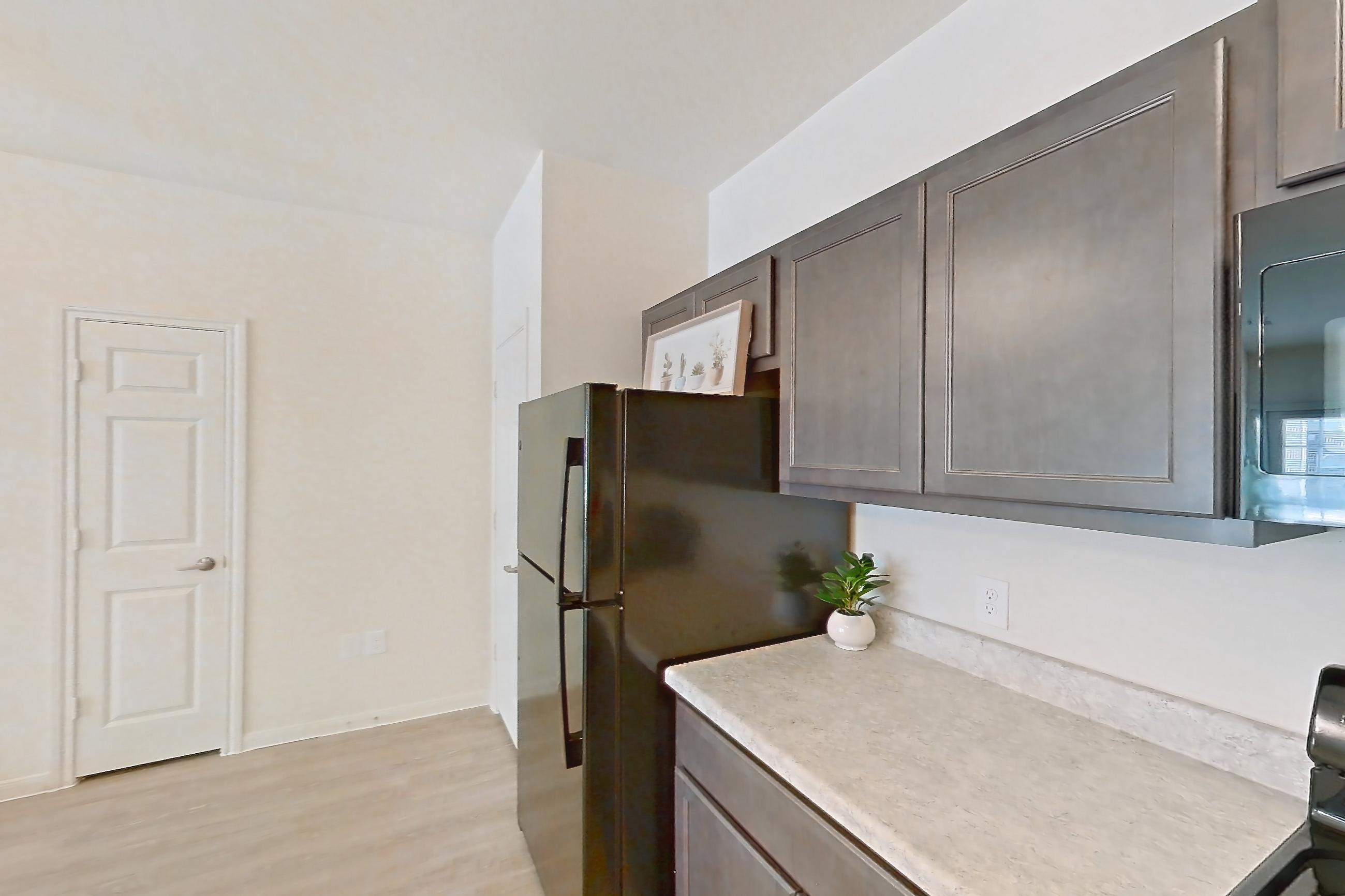 Kitchen with black appliances, dishwasher, electric range, light countertops, light wood-finish flooring, oven/range, refrigerator, and stainless steel appliances, Apartment 7103 at Mill Stream