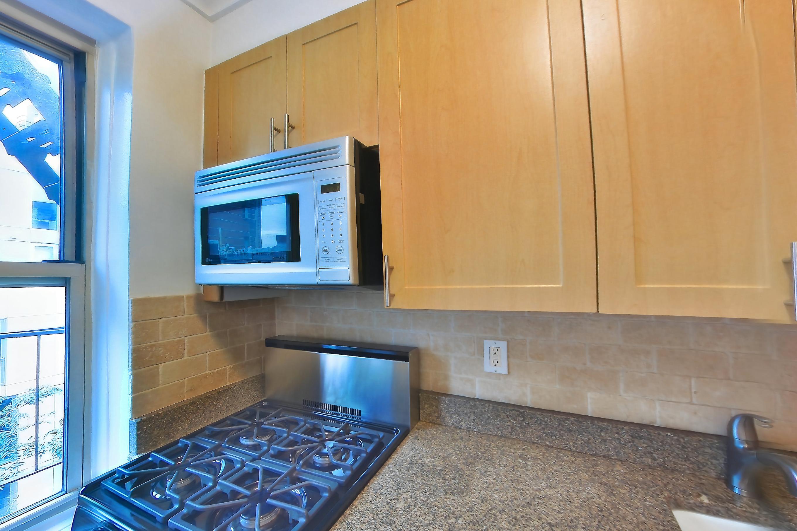 Kitchen with dark stone countertops, dishwasher, gas range, light tile flooring, microwave, oven/range, refrigerator, and stainless steel appliances, Apartment 7N at Stonehenge Leasing