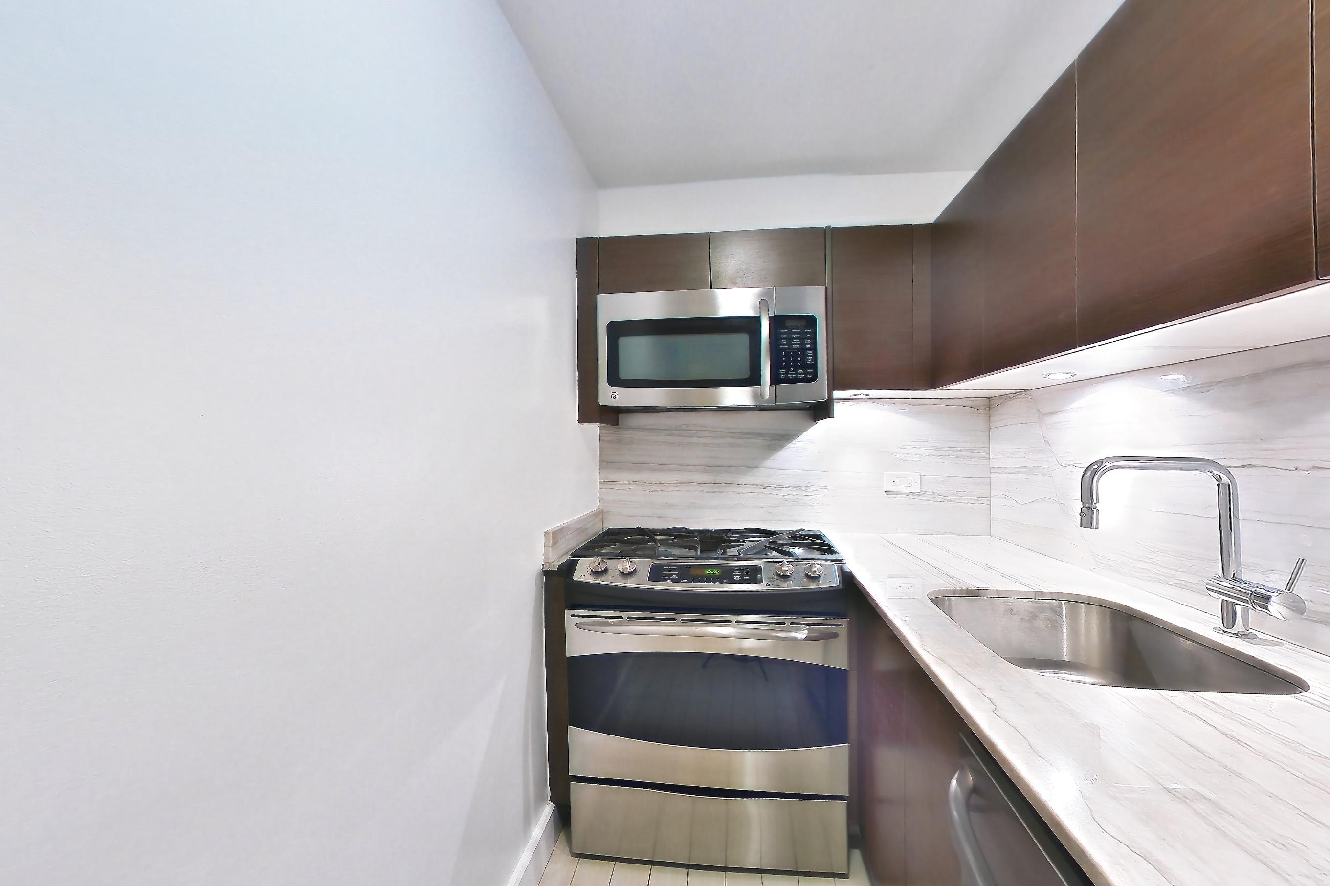 Kitchen with gas range, light countertops, light stone countertops, light wood-finish flooring, microwave, oven/range, and stainless steel appliances, Apartment 5B at Stonehenge Leasing