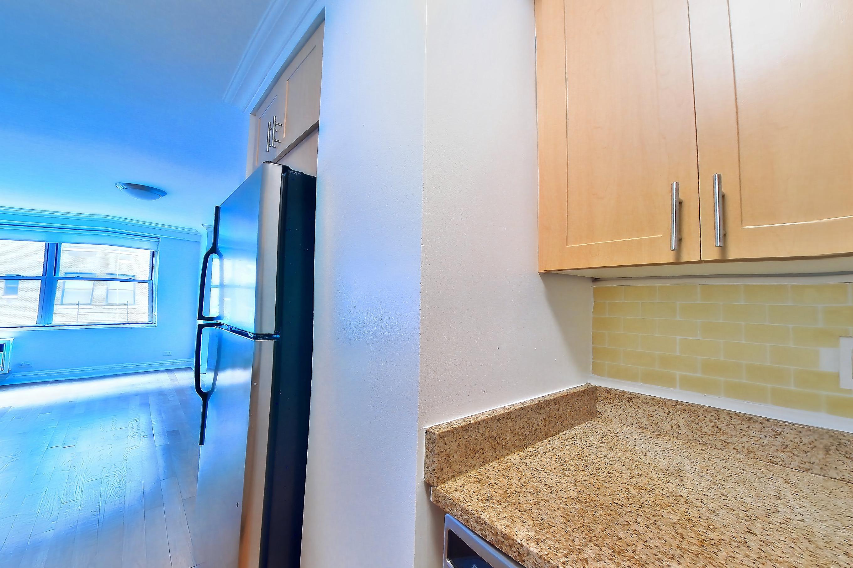 Kitchen with dishwasher, gas range, light countertops, light stone countertops, light wood-finish flooring, microwave, oven/range, and stainless steel appliances, Apartment 9G at Stonehenge Leasing