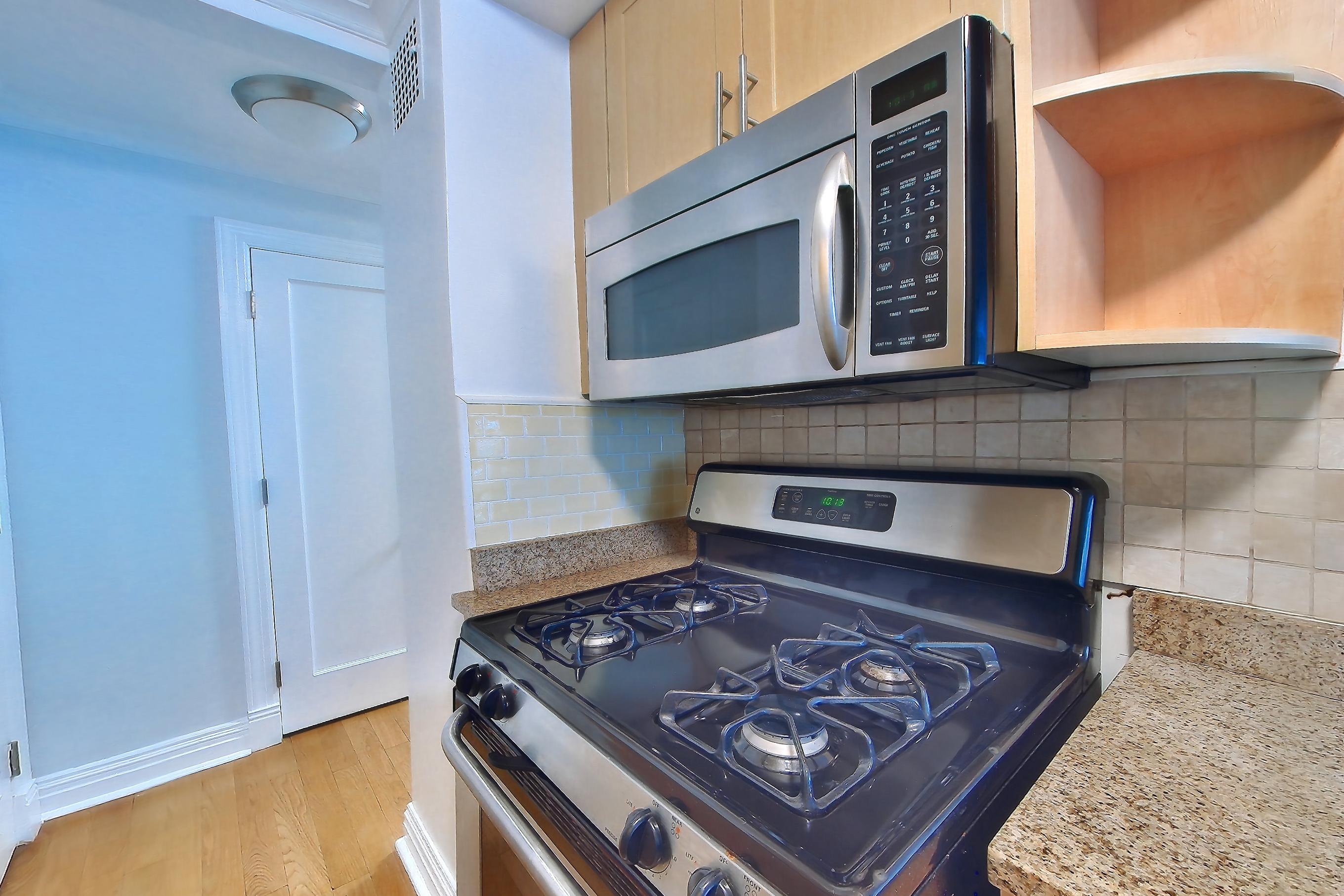Kitchen with dishwasher, gas range, light countertops, light stone countertops, light wood-finish flooring, microwave, oven/range, and stainless steel appliances, Apartment 9G at Stonehenge Leasing