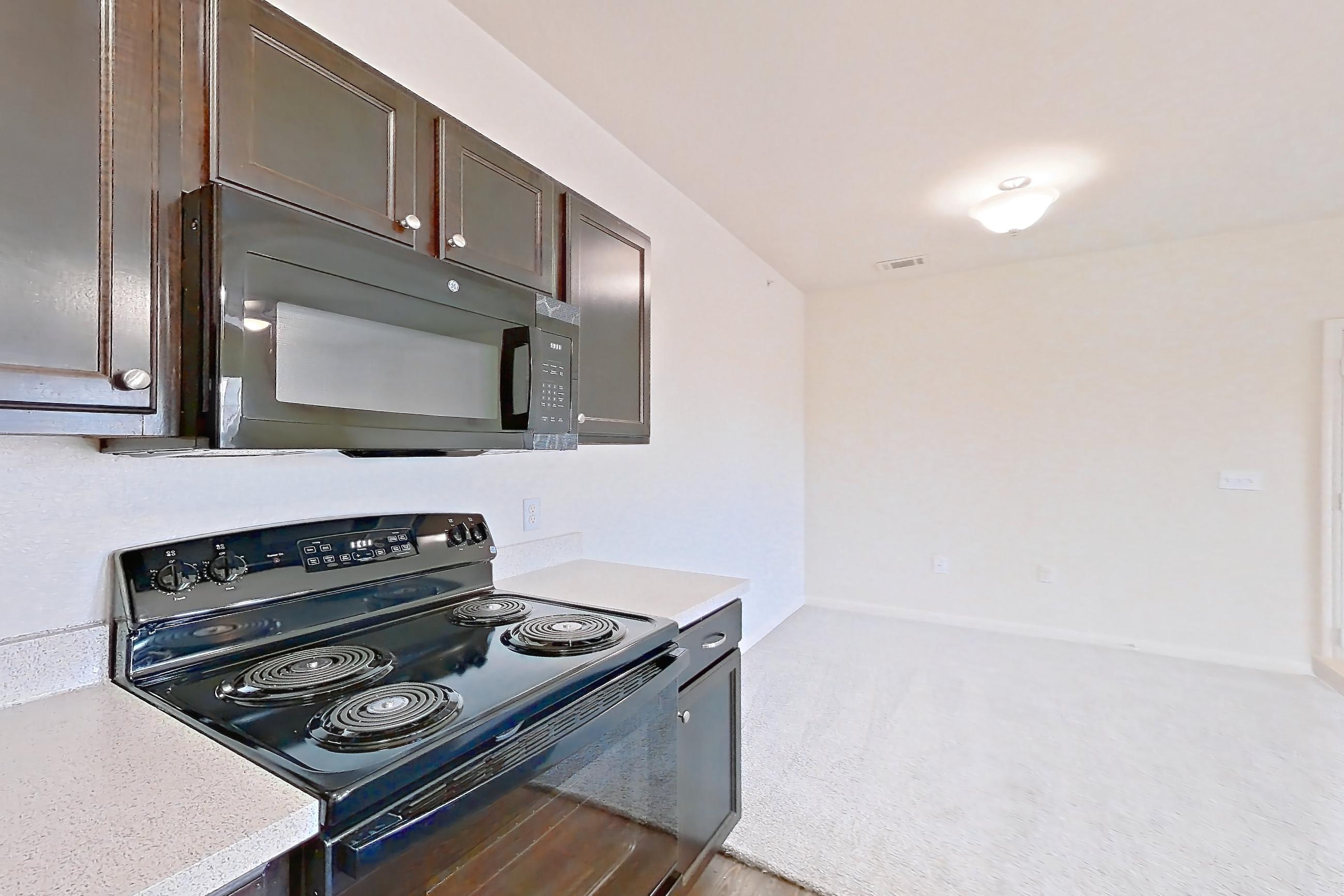 Kitchen with black appliances, dishwasher, electric range, light carpet, light countertops, light stone countertops, light wood-finish flooring, oven/range, refrigerator, and stainless steel appliances, Apartment 1231 at The Heights on Parmer