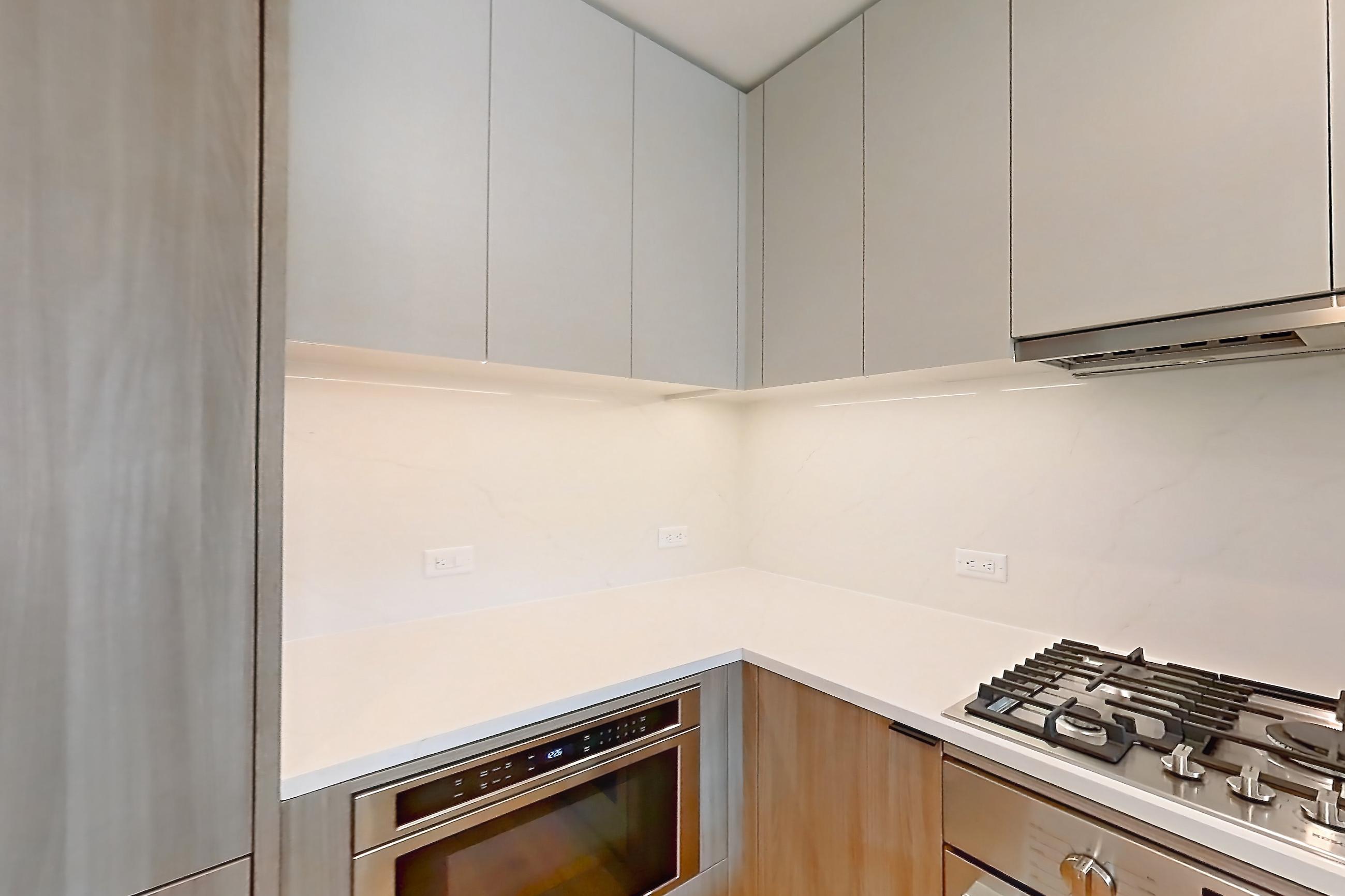 Kitchen with cooktop, gas cooktop, kitchen island, light countertops, light stone countertops, light wood-finish flooring, microwave, oven/range, and stainless steel appliances, Apartment 03D at Maison 78