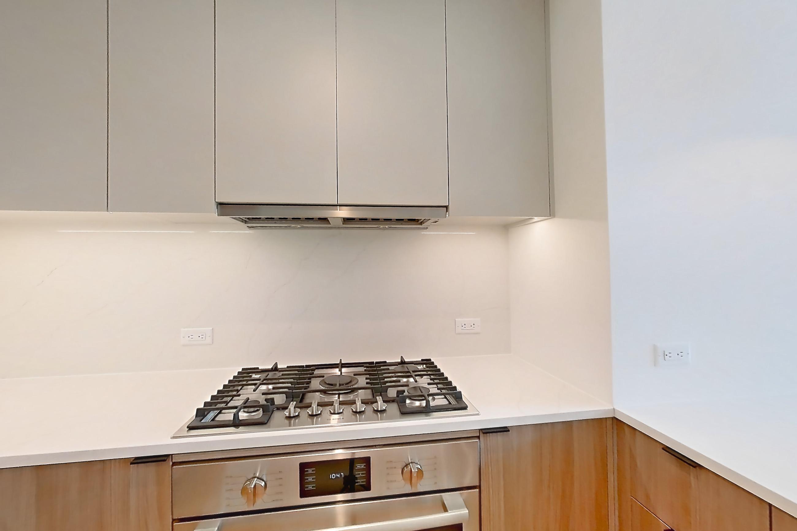 Kitchen with cooktop, gas cooktop, kitchen island, light countertops, light stone countertops, light wood-finish flooring, microwave, oven/range, and stainless steel appliances, Apartment 03D at Maison 78