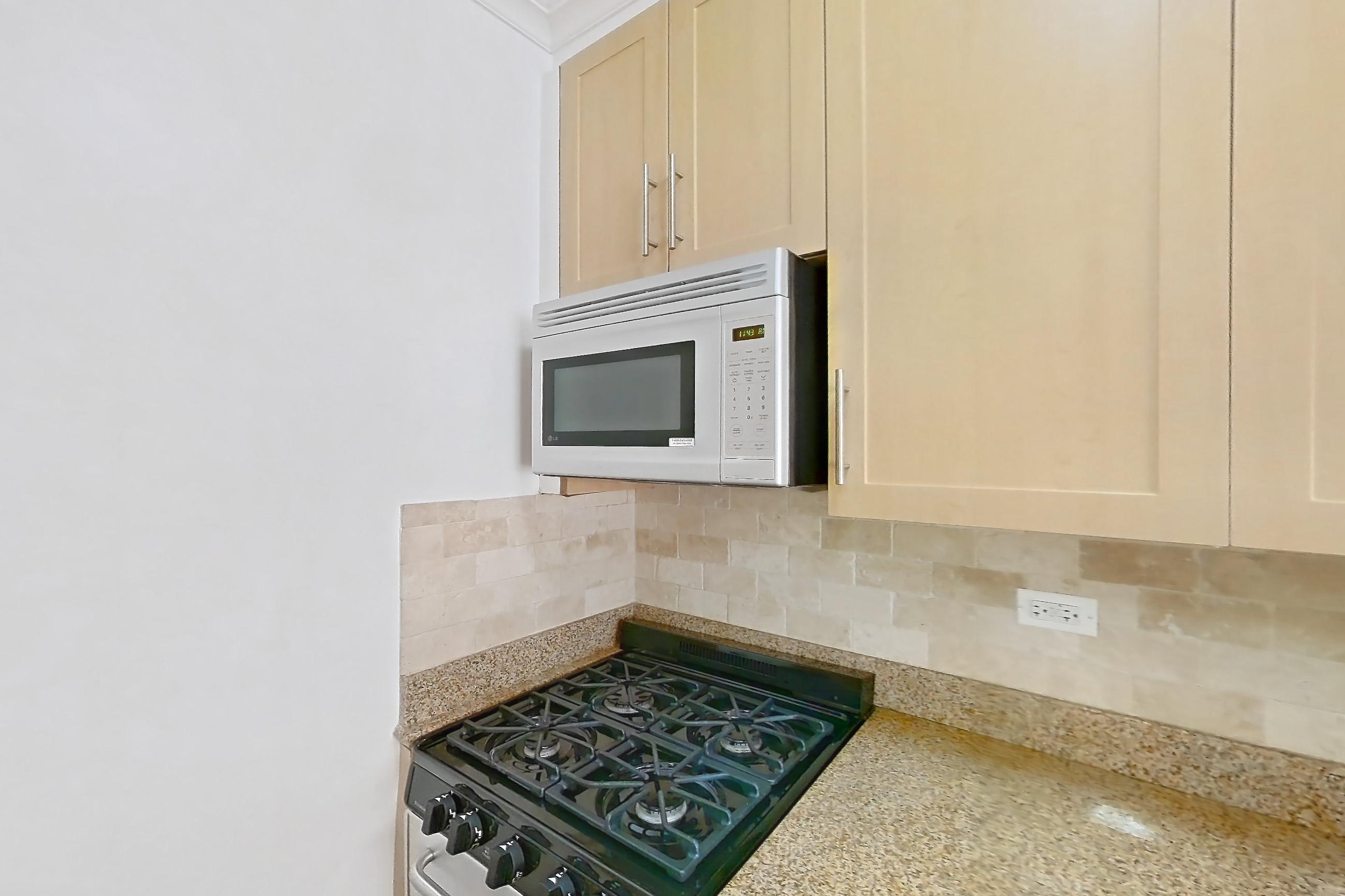 Kitchen with dishwasher, gas range, light countertops, light stone countertops, light wood-finish flooring, microwave, oven/range, refrigerator, stainless steel appliances, and white appliances, Apartment 6F at Stonehenge Leasing