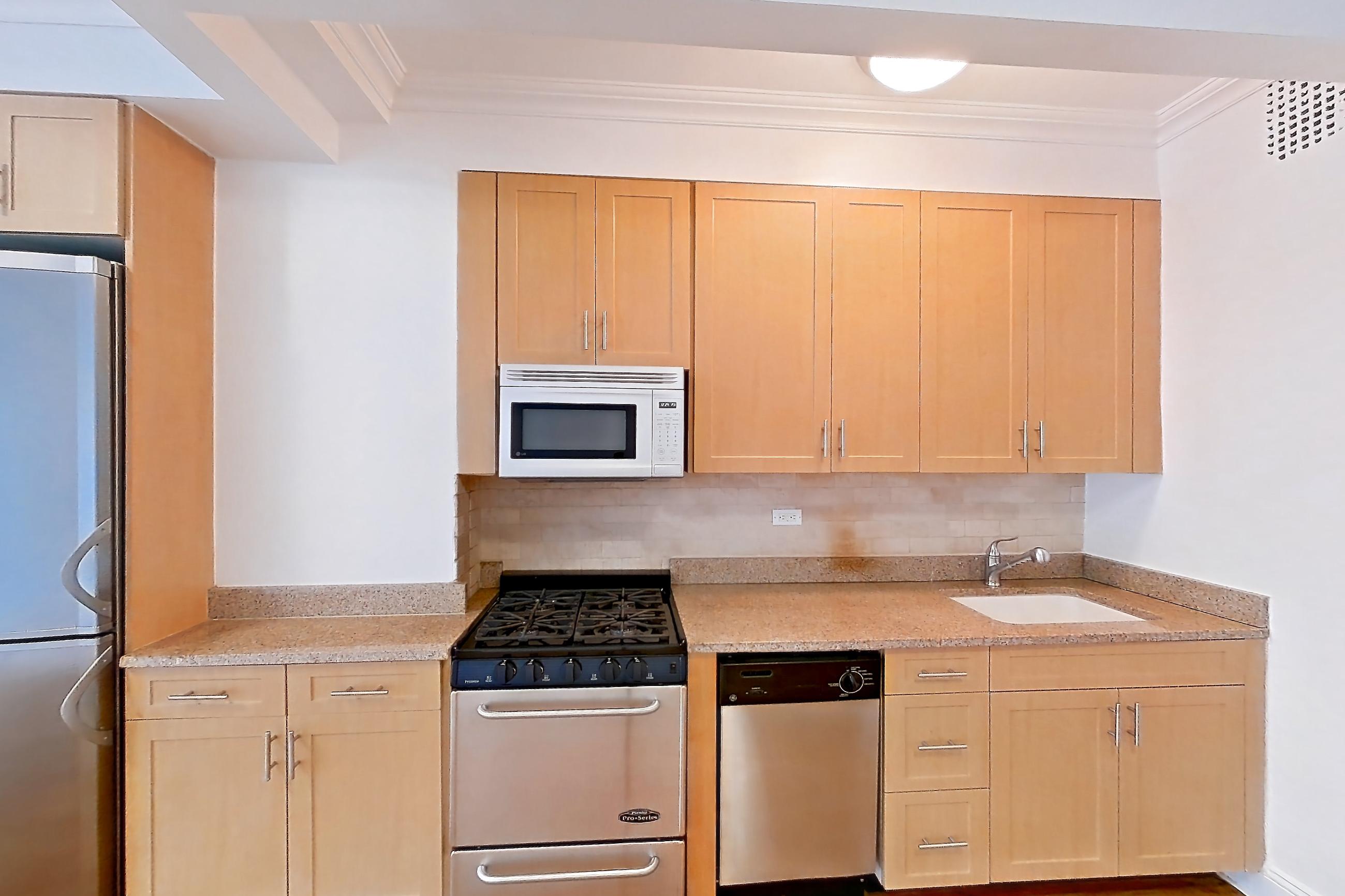 Kitchen with dishwasher, gas range, light countertops, light stone countertops, light wood-finish flooring, microwave, oven/range, refrigerator, stainless steel appliances, and white appliances, Apartment 9G at Stonehenge Leasing