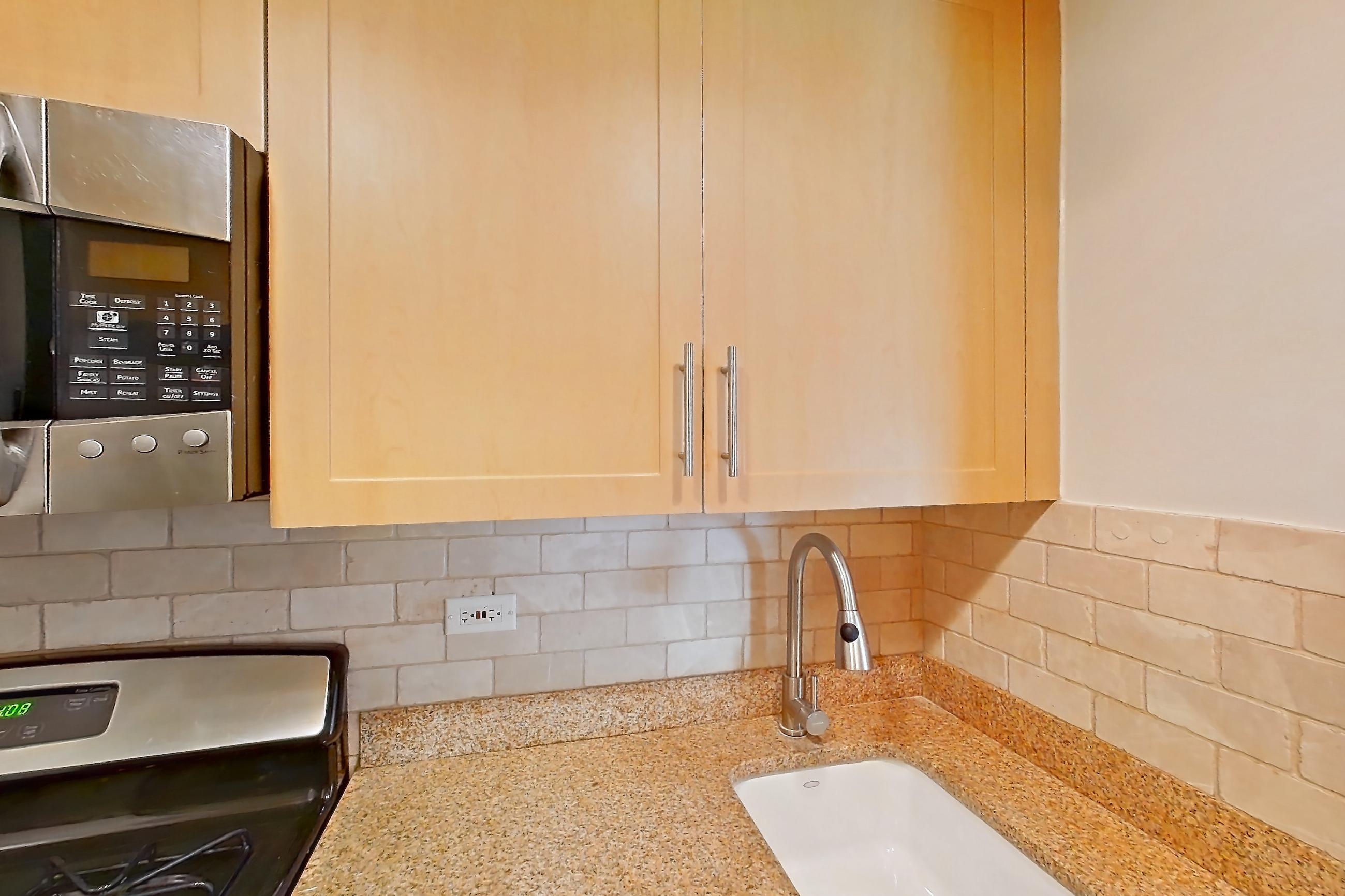 Kitchen with black appliances, dishwasher, gas range, light countertops, light stone countertops, light tile flooring, microwave, oven/range, and stainless steel appliances, Apartment 11D at Stonehenge Leasing