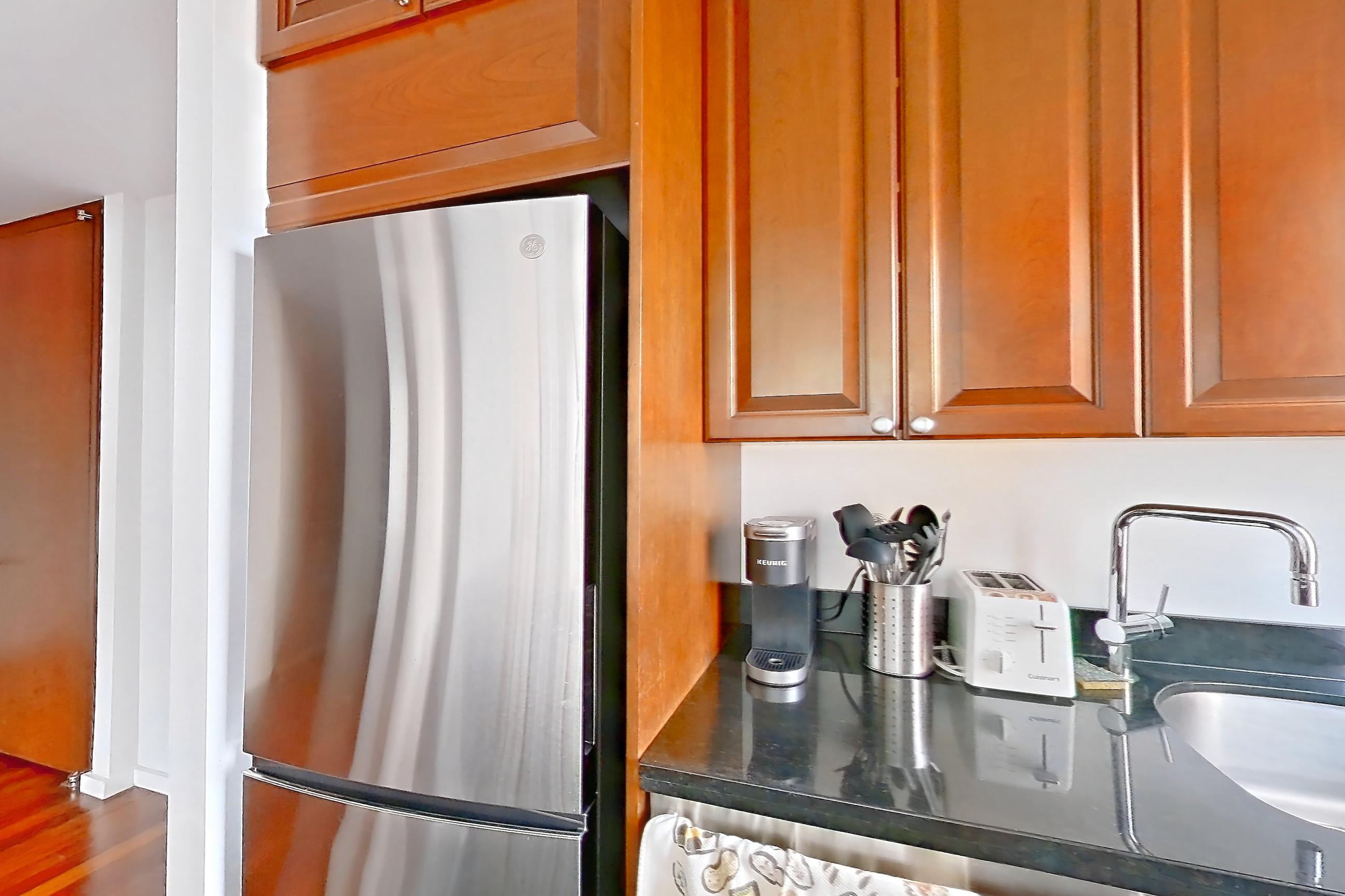 Kitchen with black appliances, cooktop, dark stone countertops, dark tile flooring, dishwasher, gas cooktop, light countertops, refrigerator, and stainless steel appliances, Apartment 43L at Stonehenge Leasing