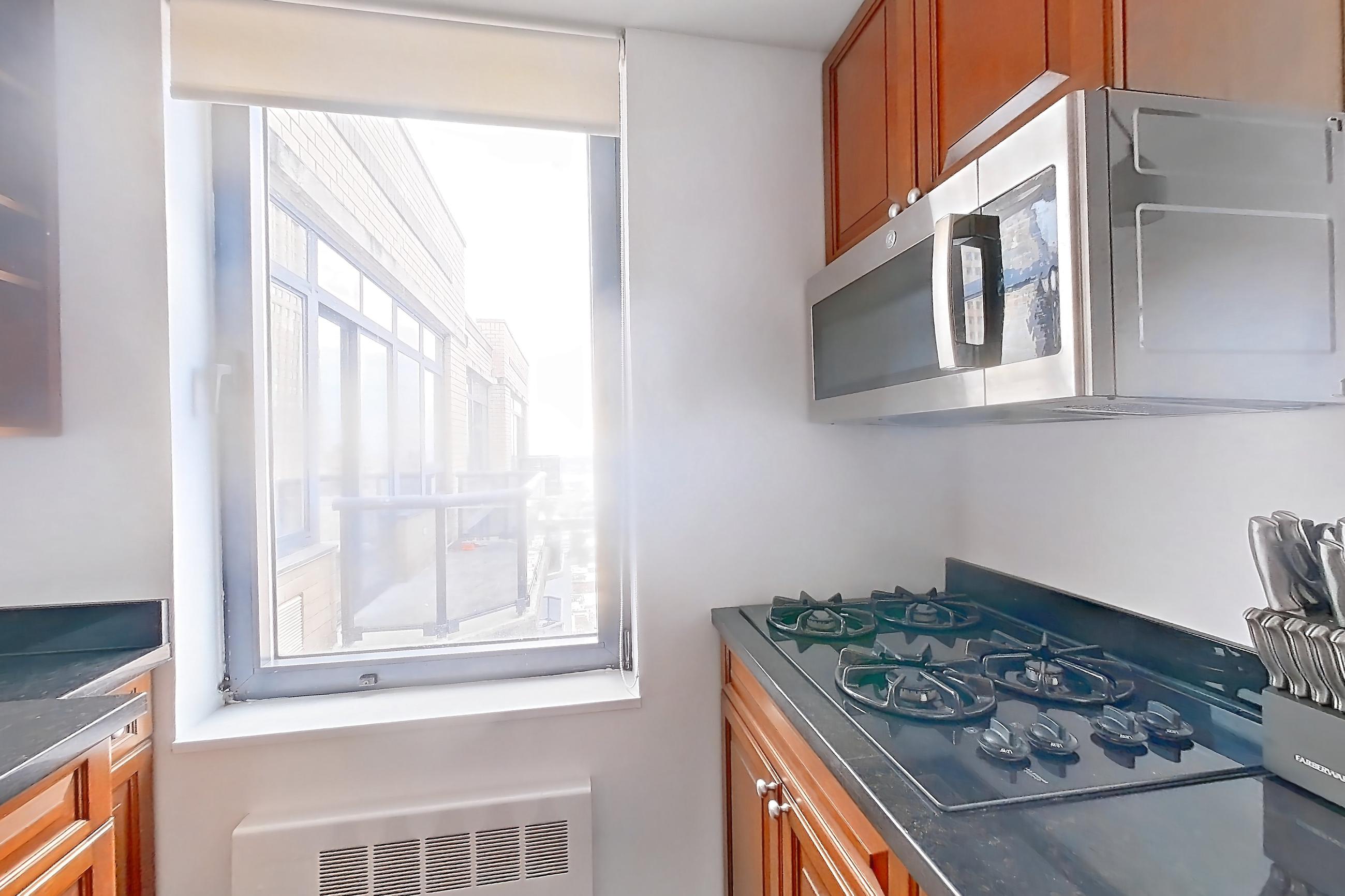 Kitchen with black appliances, cooktop, dark stone countertops, dark tile flooring, dishwasher, gas cooktop, light countertops, refrigerator, and stainless steel appliances, Apartment 43L at Stonehenge Leasing