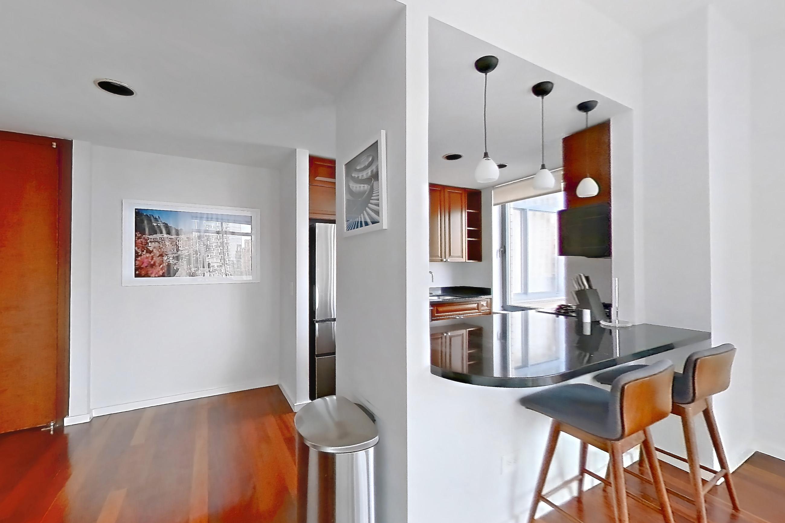 Living room with dark countertops, dark wood-finish flooring, refrigerator, and stainless steel appliances, Apartment 43L at Stonehenge Leasing