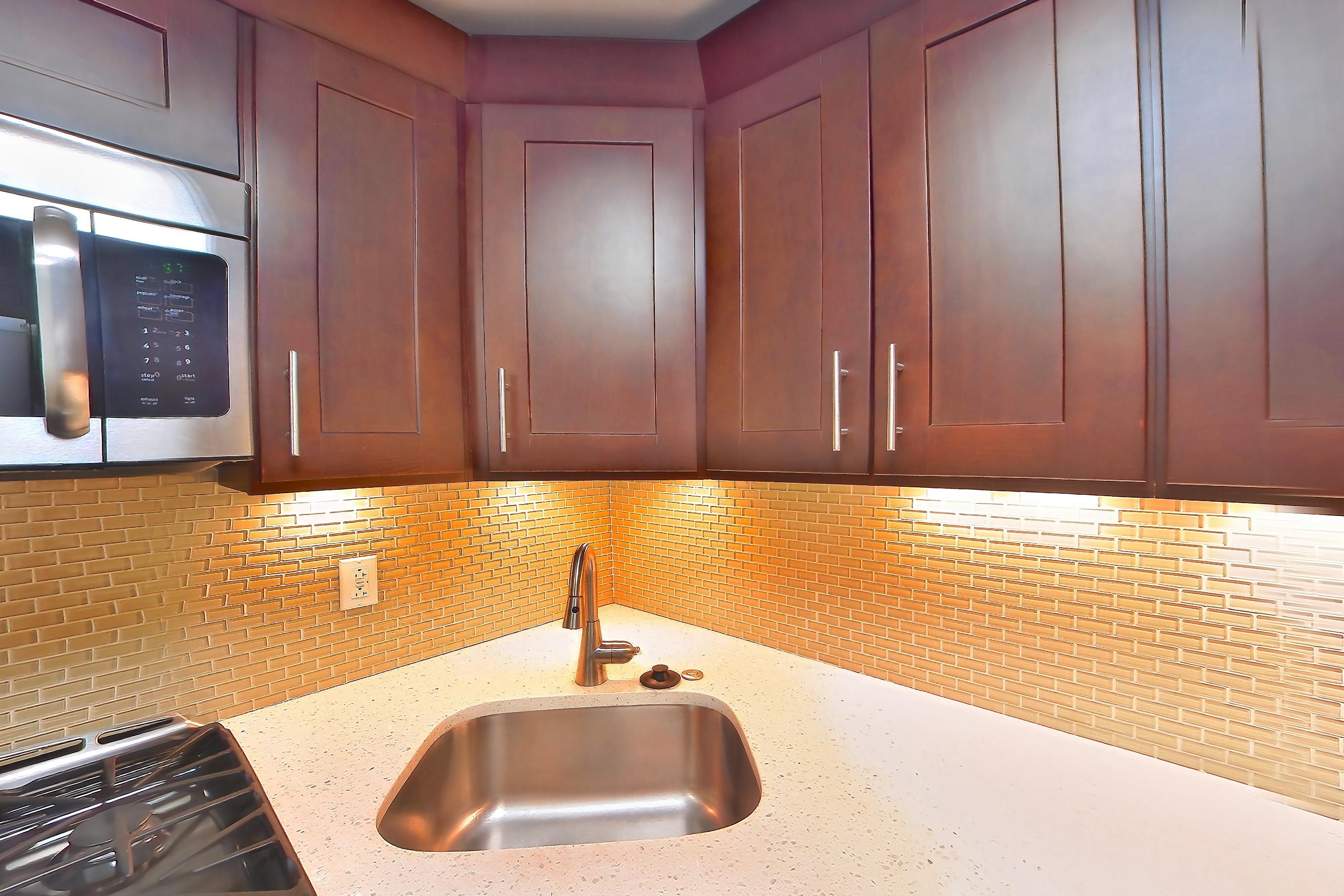 Kitchen with dark wood-finish flooring, dishwasher, gas range, light countertops, light stone countertops, microwave, oven/range, and stainless steel appliances, Apartment 403 at Stonehenge Leasing