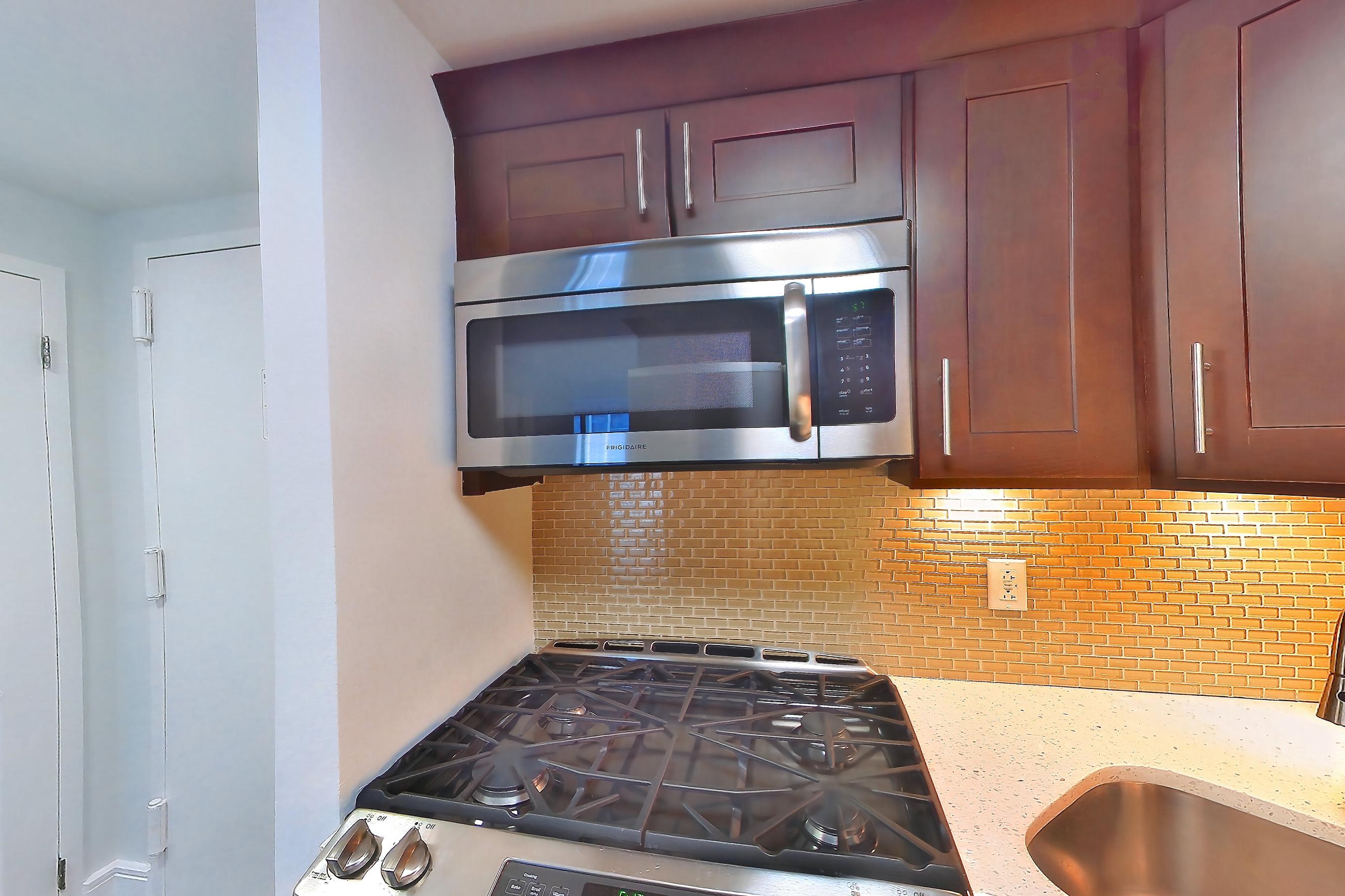 Kitchen with dark wood-finish flooring, dishwasher, gas range, light countertops, light stone countertops, microwave, oven/range, and stainless steel appliances, Apartment 403 at Stonehenge Leasing