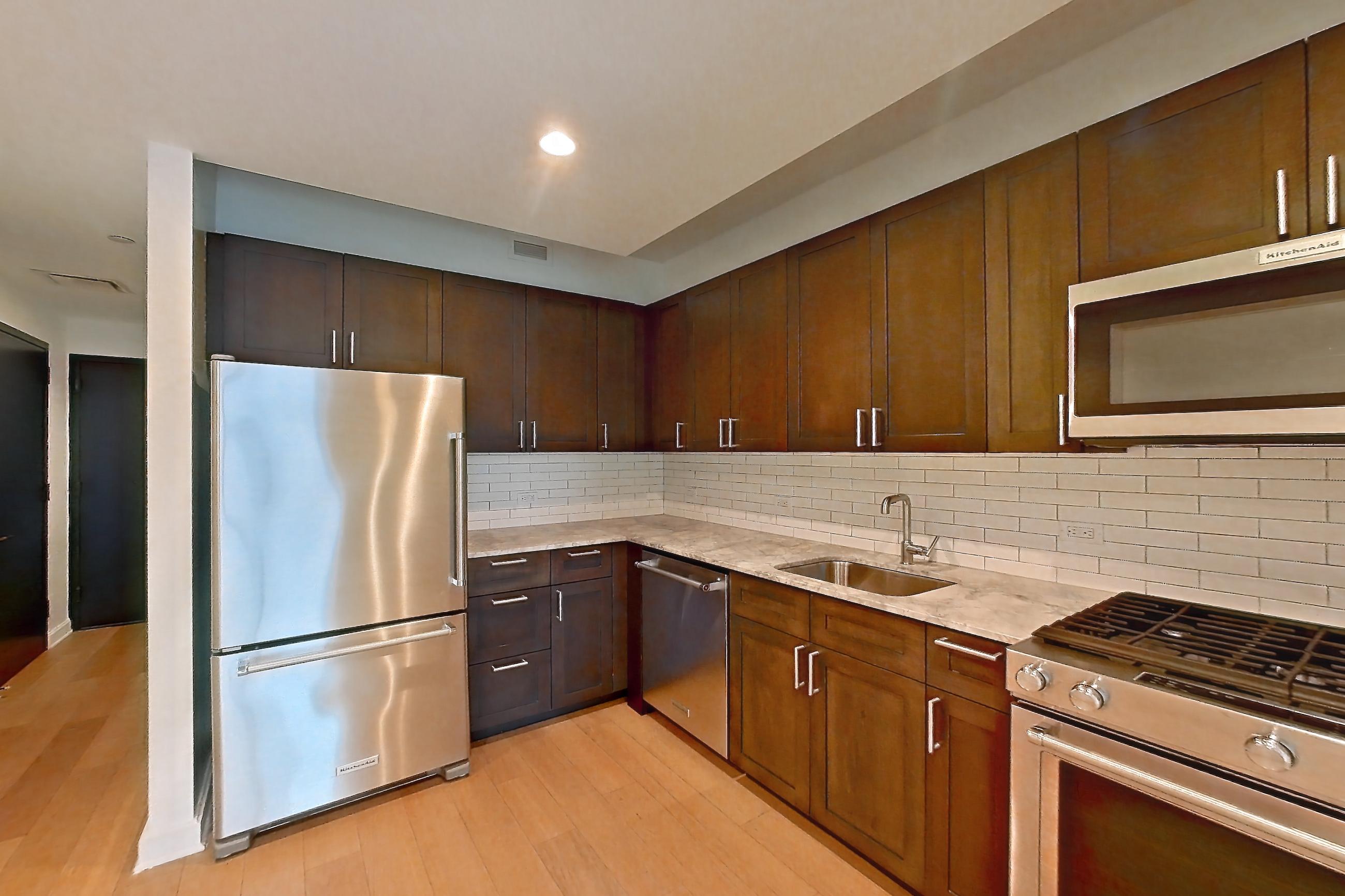 Kitchen with dishwasher, gas range, light countertops, light stone countertops, light wood-finish flooring, microwave, oven/range, refrigerator, and stainless steel appliances, Apartment 1915 at 21 West End Avenue