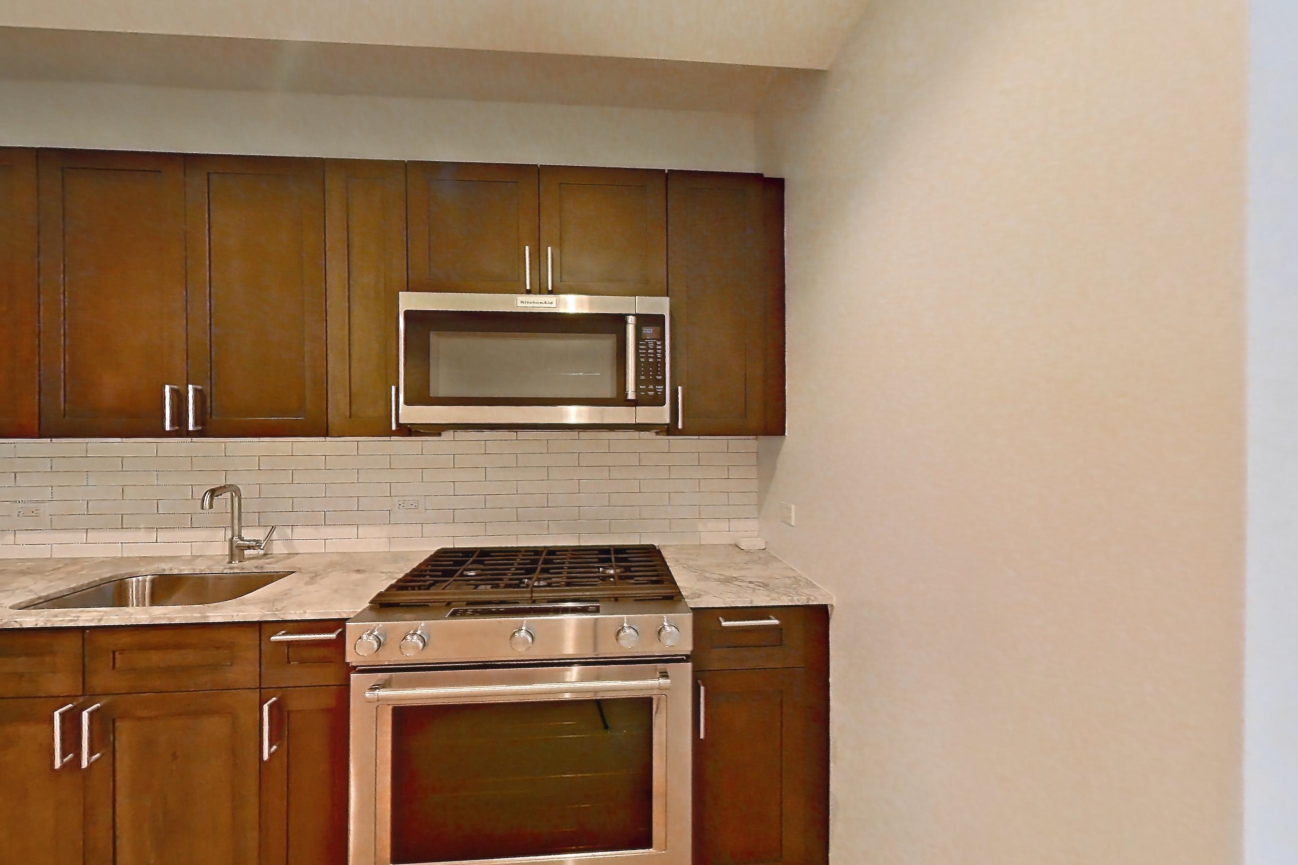 Kitchen with dishwasher, gas range, light countertops, light stone countertops, light wood-finish flooring, microwave, oven/range, refrigerator, and stainless steel appliances, Apartment 1915 at 21 West End Avenue