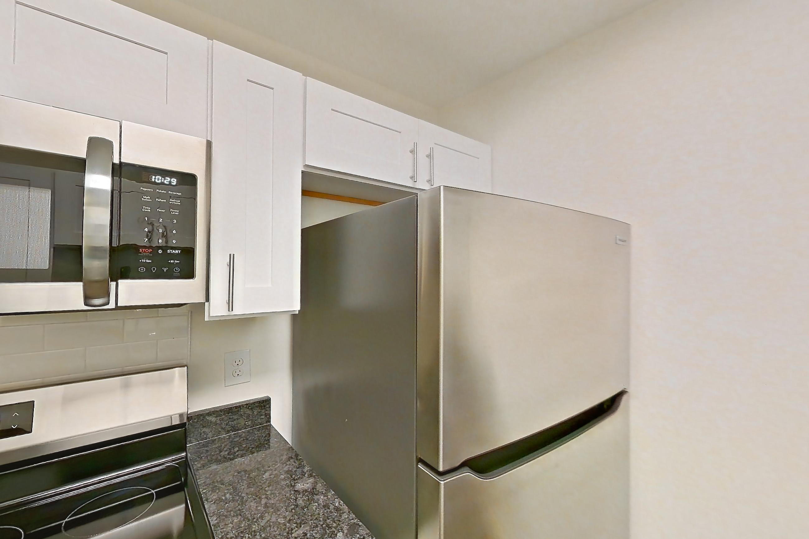Kitchen with dark stone countertops, dark wood-finish flooring, electric range, light countertops, light wood-finish flooring, microwave, oven/range, refrigerator, and stainless steel appliances, Apartment 68108 at The Boulders