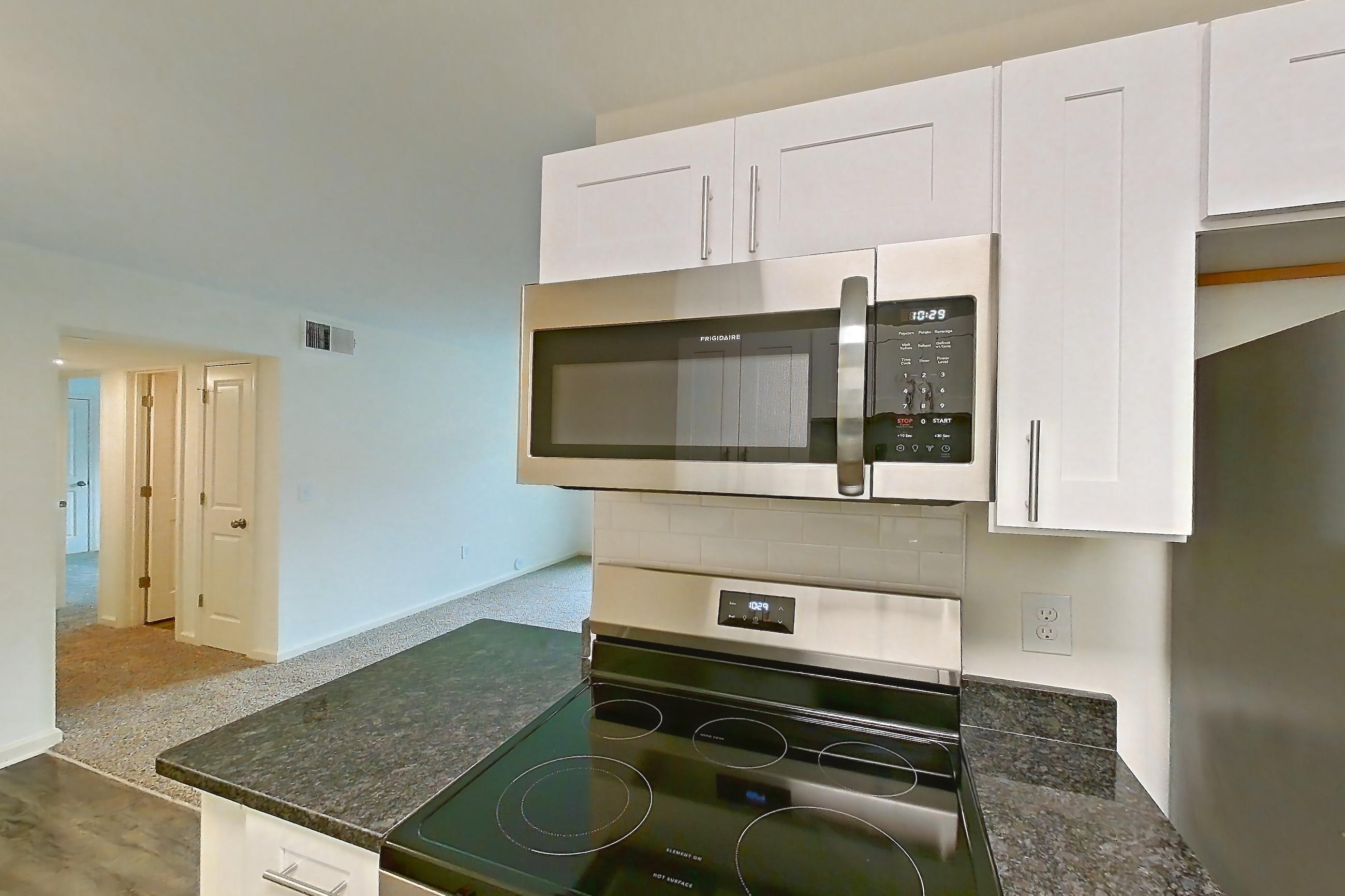 Kitchen with dark stone countertops, dark wood-finish flooring, electric range, light countertops, light wood-finish flooring, microwave, oven/range, refrigerator, and stainless steel appliances, Apartment 68108 at The Boulders