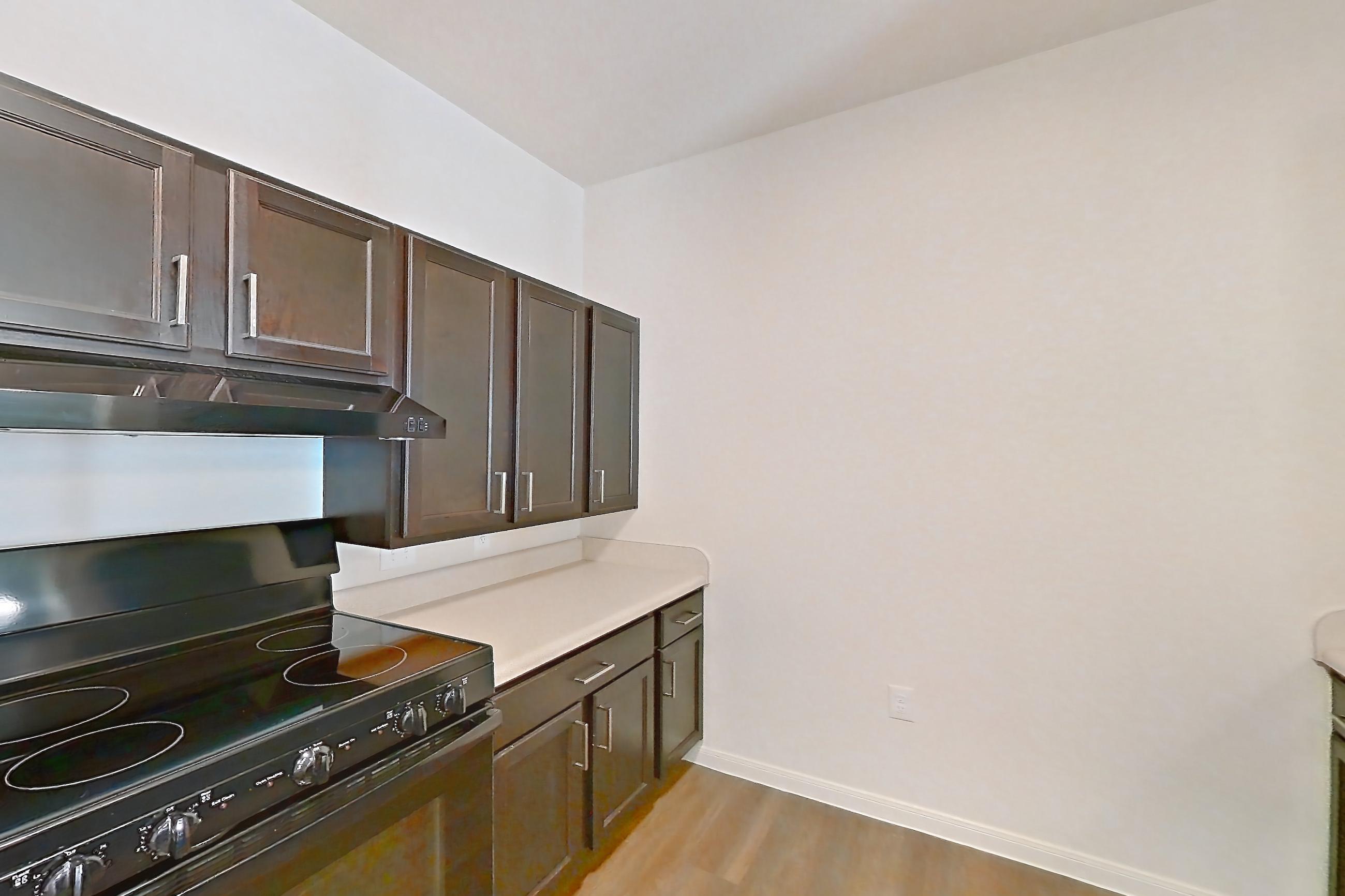 Kitchen with black appliances, dark wood-finish flooring, dishwasher, light countertops, light wood-finish flooring, microwave, oven/range, refrigerator, and stainless steel appliances, Apartment 11105 at Canyon Pass