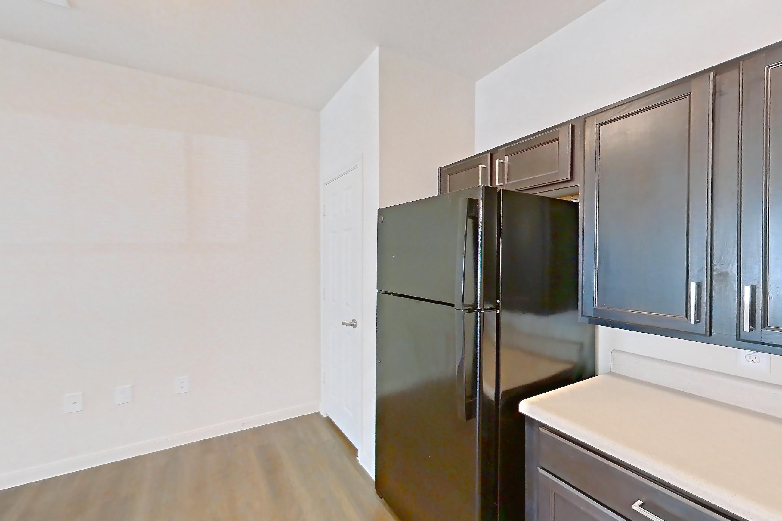Kitchen with black appliances, dark wood-finish flooring, dishwasher, light countertops, light wood-finish flooring, microwave, oven/range, refrigerator, and stainless steel appliances, Apartment 11105 at Canyon Pass