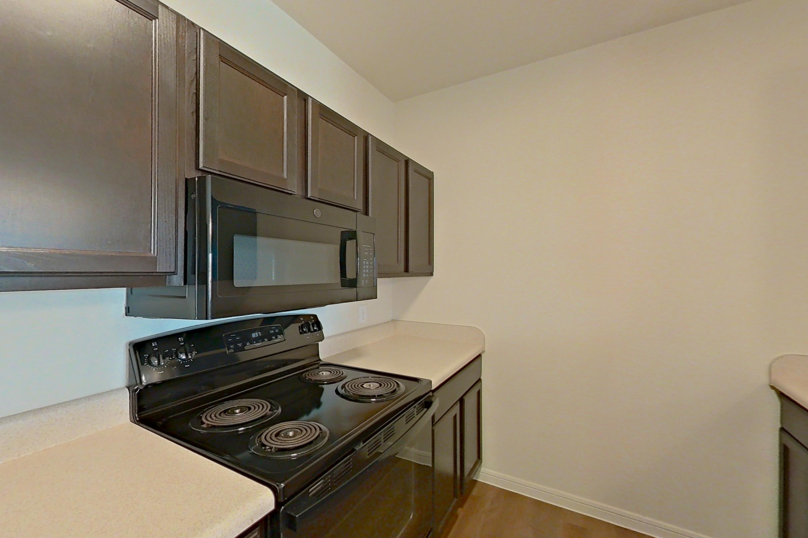 Kitchen with black appliances, dishwasher, electric range, light countertops, light wood-finish flooring, oven/range, refrigerator, and stainless steel appliances, Apartment 9301 at Canyon Pass