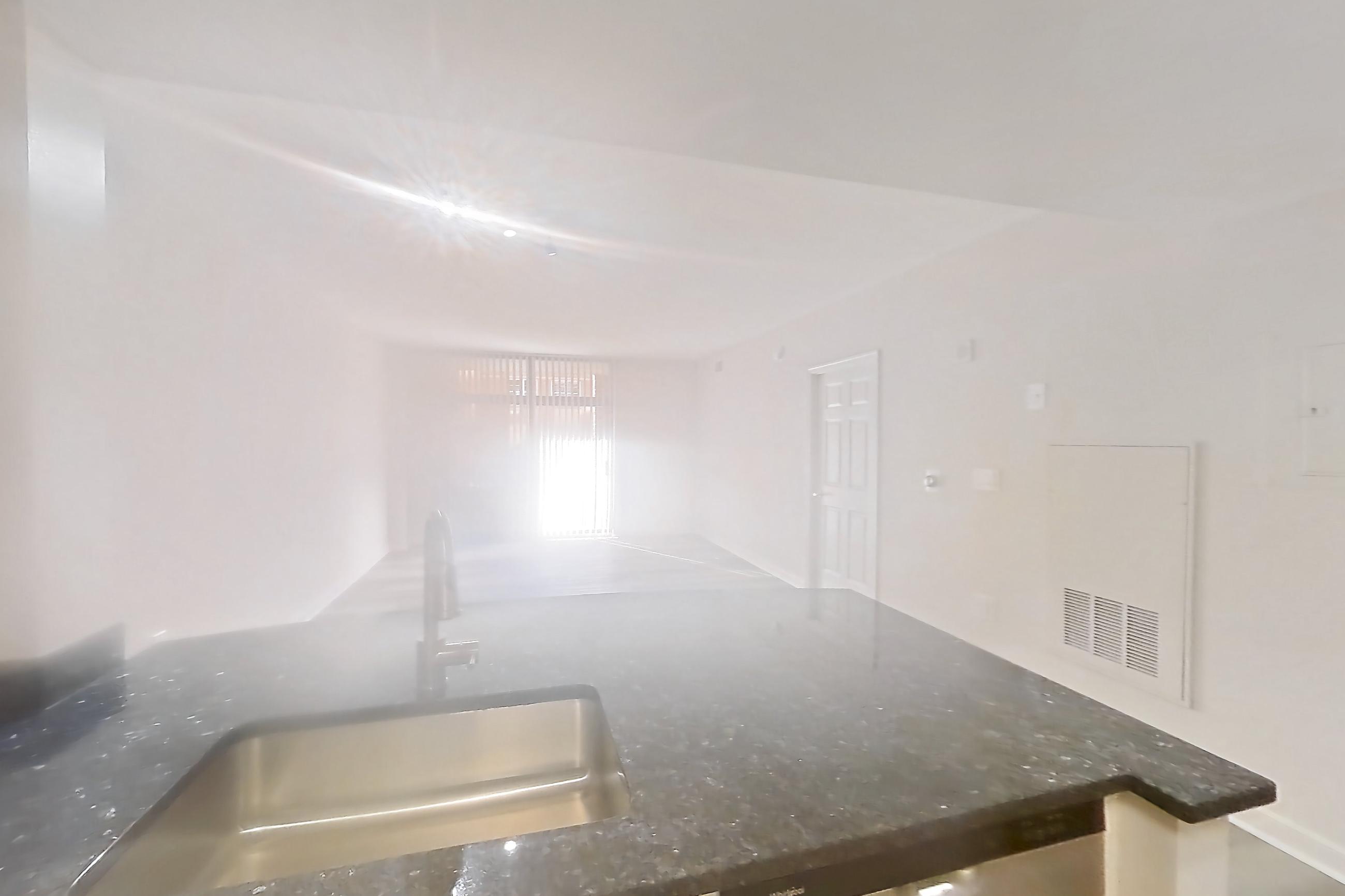 Kitchen with dark stone countertops, dishwasher, gas range, light countertops, light wood-finish flooring, oven/range, refrigerator, and stainless steel appliances, Apartment 405 at The Barton at Woodley