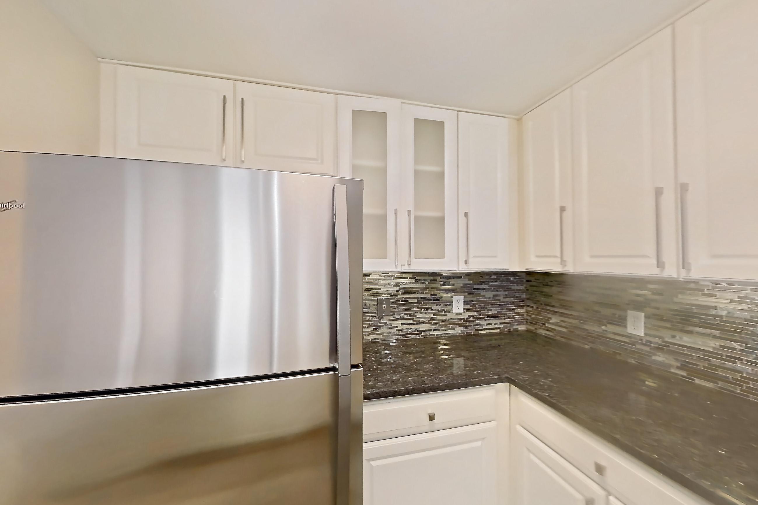 Kitchen with dark stone countertops, dishwasher, gas range, light countertops, light wood-finish flooring, oven/range, refrigerator, and stainless steel appliances, Apartment 405 at The Barton at Woodley