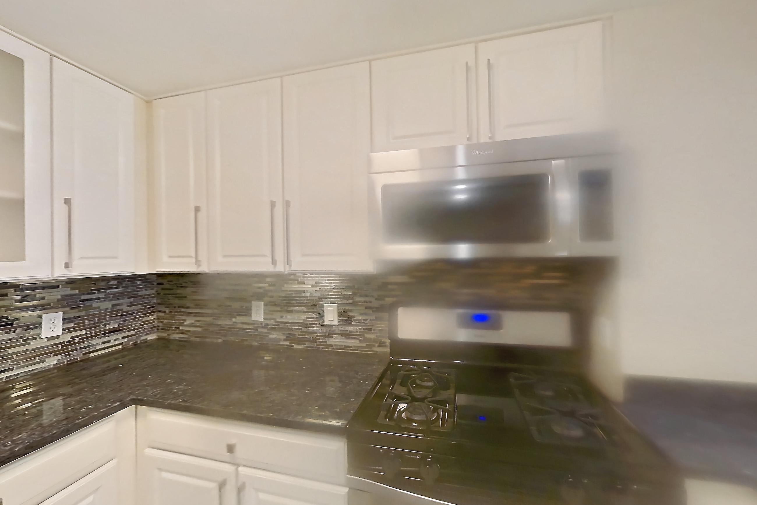 Kitchen with dark stone countertops, dishwasher, gas range, light countertops, light wood-finish flooring, oven/range, refrigerator, and stainless steel appliances, Apartment 405 at The Barton at Woodley