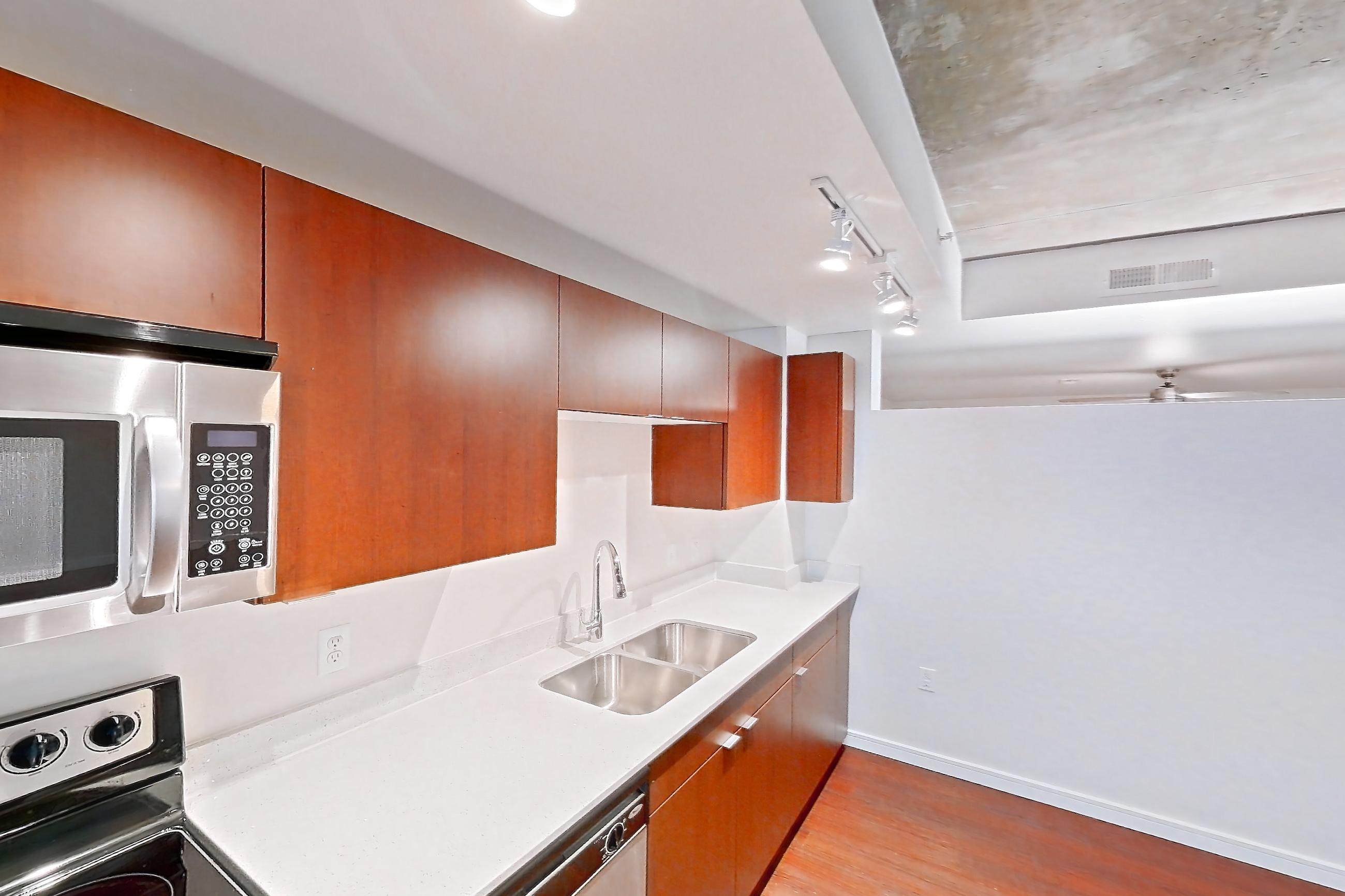 Kitchen with black appliances, dark wood-finish flooring, dishwasher, electric range, light countertops, light stone countertops, light wood-finish flooring, microwave, oven/range, refrigerator, and stainless steel appliances, Apartment 301 at Solera