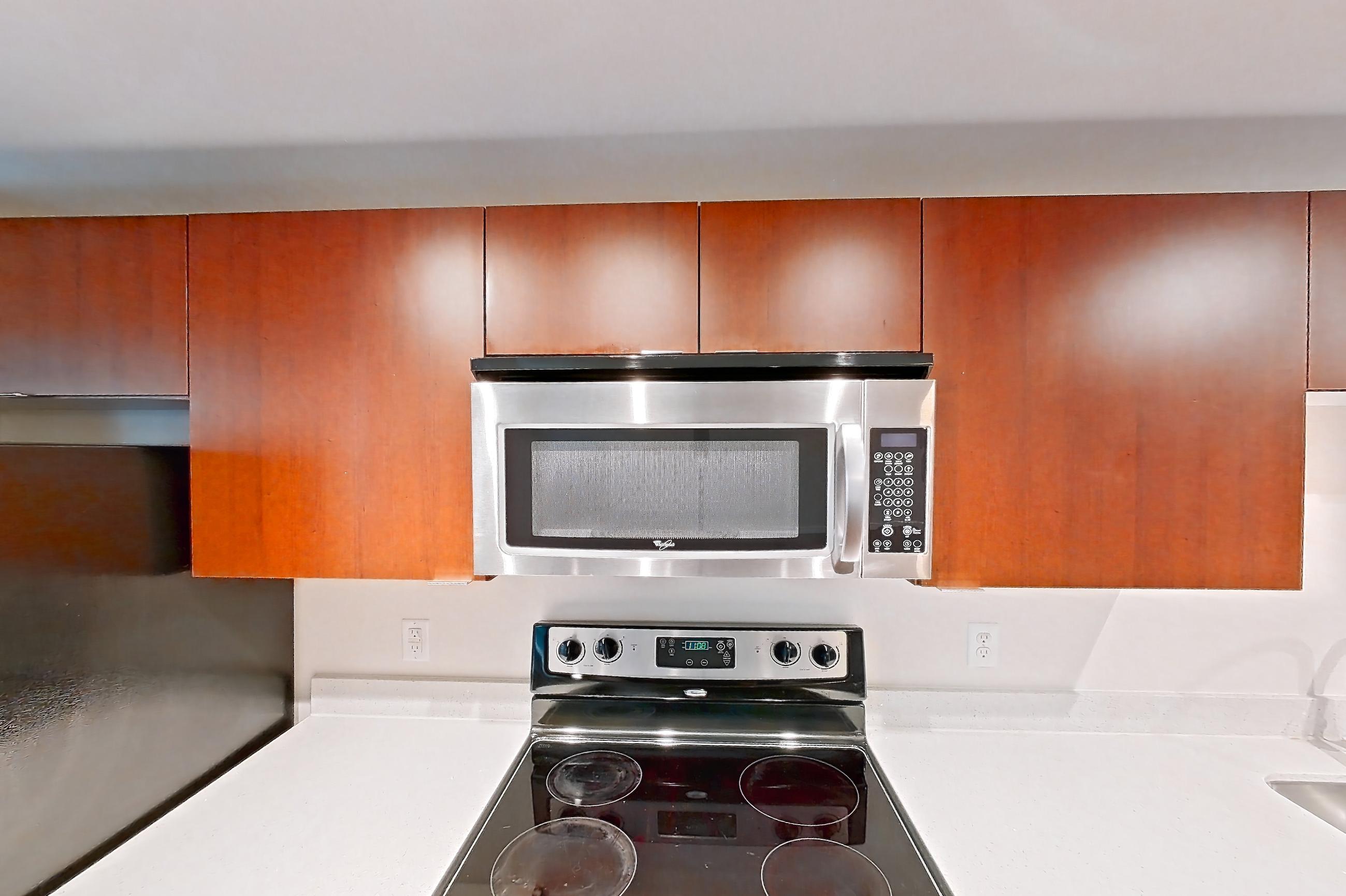 Kitchen with black appliances, dark wood-finish flooring, dishwasher, electric range, light countertops, light stone countertops, light wood-finish flooring, microwave, oven/range, refrigerator, and stainless steel appliances, Apartment 301 at Solera