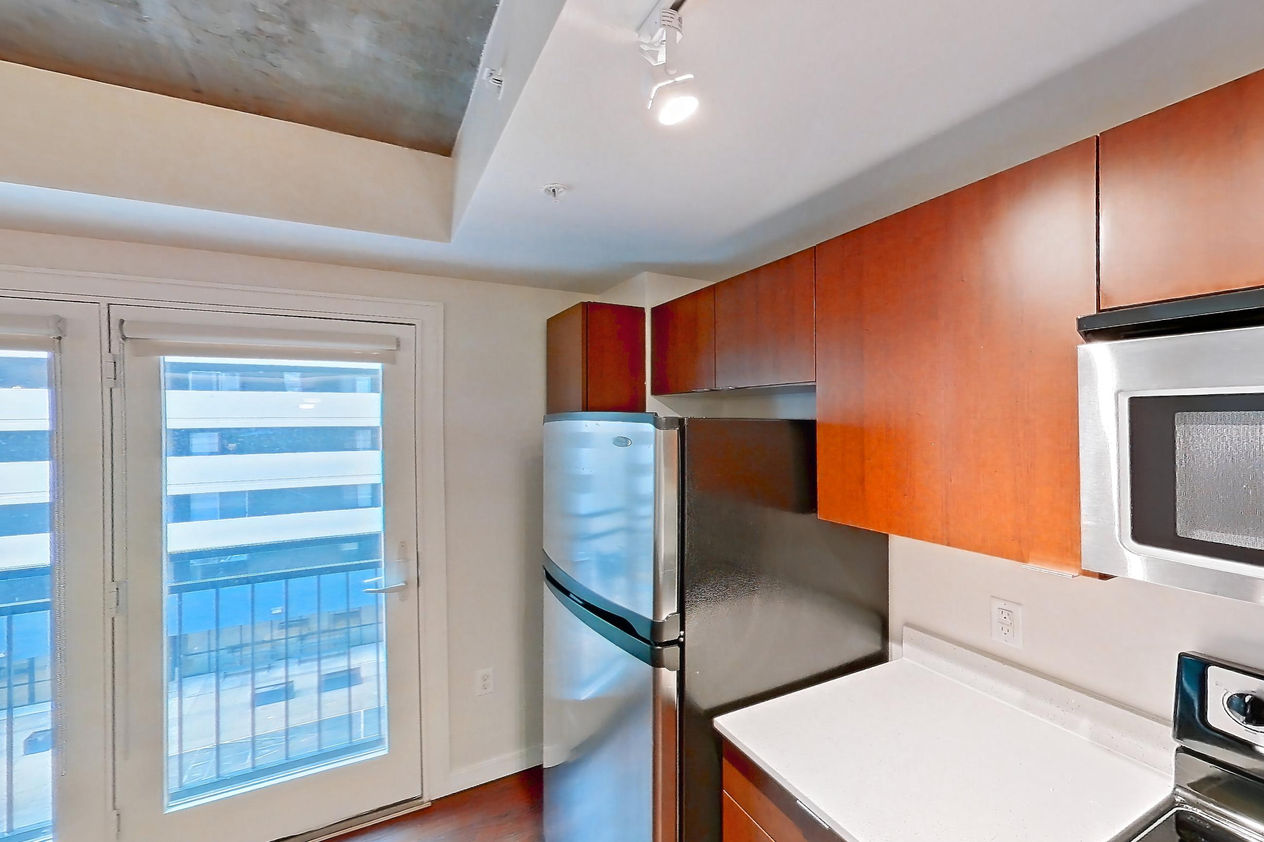 Kitchen with black appliances, dark wood-finish flooring, dishwasher, electric range, light countertops, light stone countertops, light wood-finish flooring, microwave, oven/range, refrigerator, and stainless steel appliances, Apartment 301 at Solera