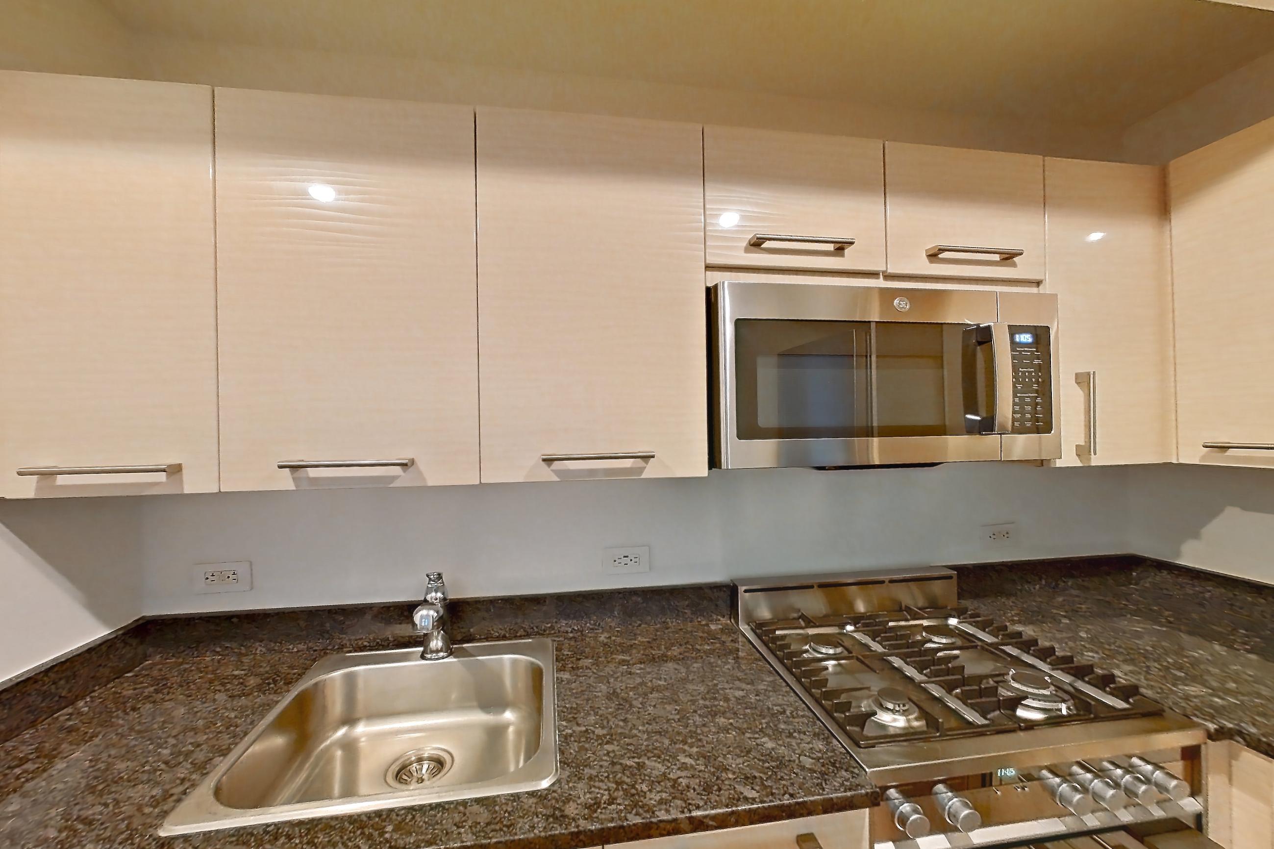 Kitchen with cooktop, dark stone countertops, gas cooktop, gas range, light countertops, light wood-finish flooring, microwave, oven/range, parquet flooring, refrigerator, and stainless steel appliances, Apartment 419 at 20 Exchange Place