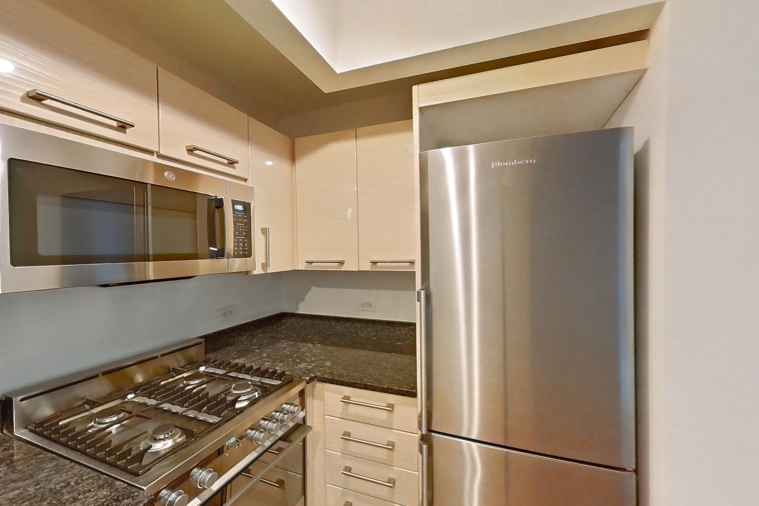 Kitchen with cooktop, dark stone countertops, gas cooktop, gas range, light countertops, light wood-finish flooring, microwave, oven/range, parquet flooring, refrigerator, and stainless steel appliances, Apartment 419 at 20 Exchange Place