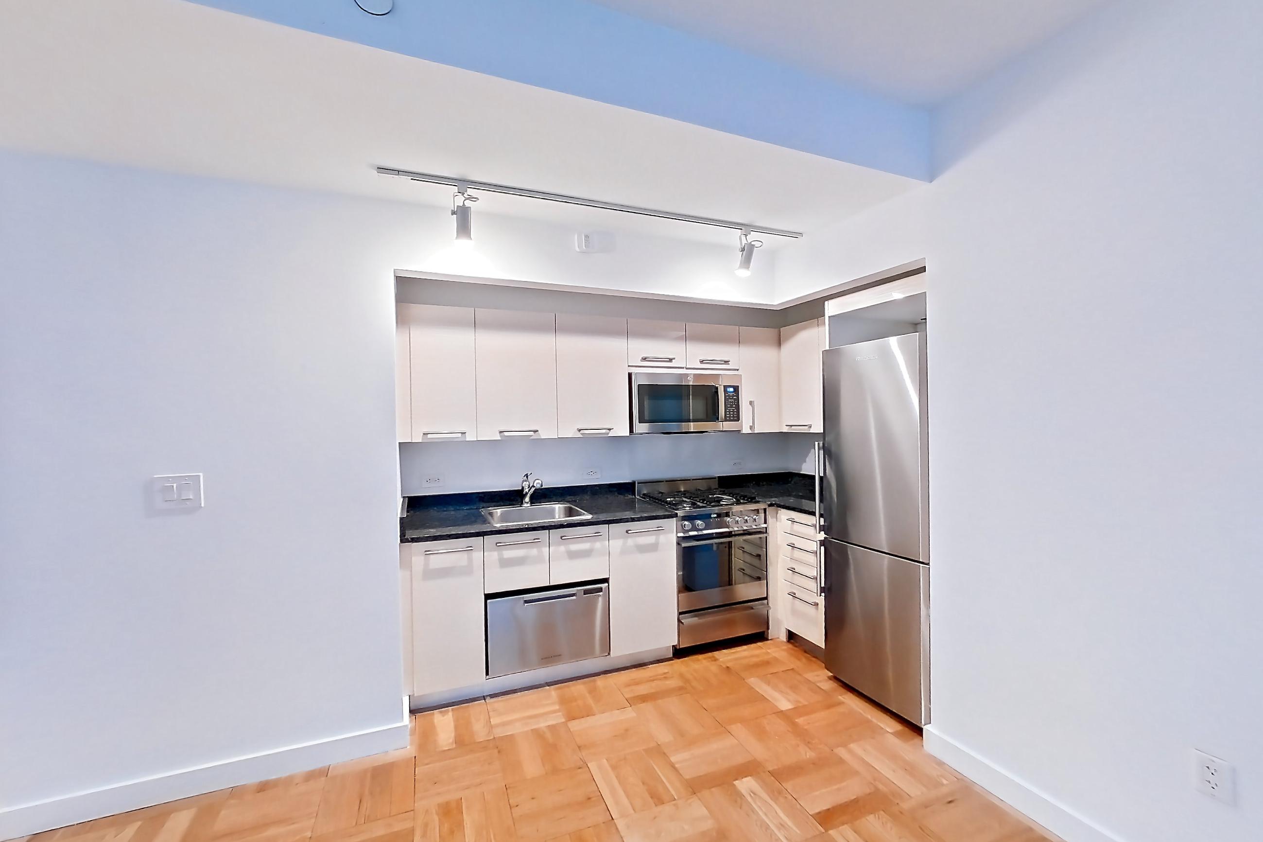 Living space with dark stone countertops, gas range, light countertops, light wood-finish flooring, microwave, oven/range, parquet flooring, refrigerator, and stainless steel appliances, Apartment 419 at 20 Exchange Place