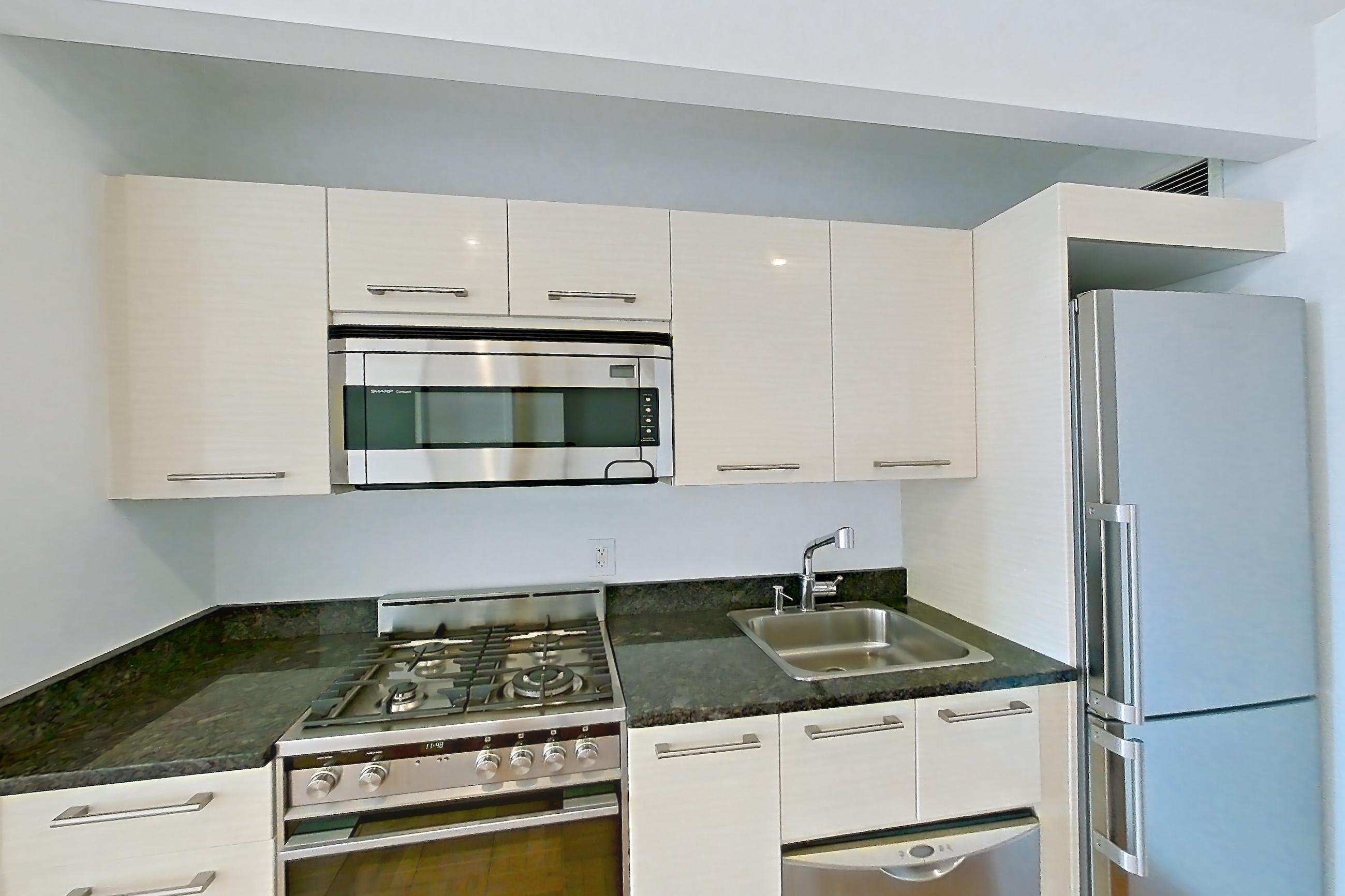 Kitchen with dark stone countertops, dishwasher, gas range, light countertops, light wood-finish flooring, microwave, oven/range, parquet flooring, refrigerator, stainless steel appliances, and white appliances, Apartment 2906 at 20 Exchange Place